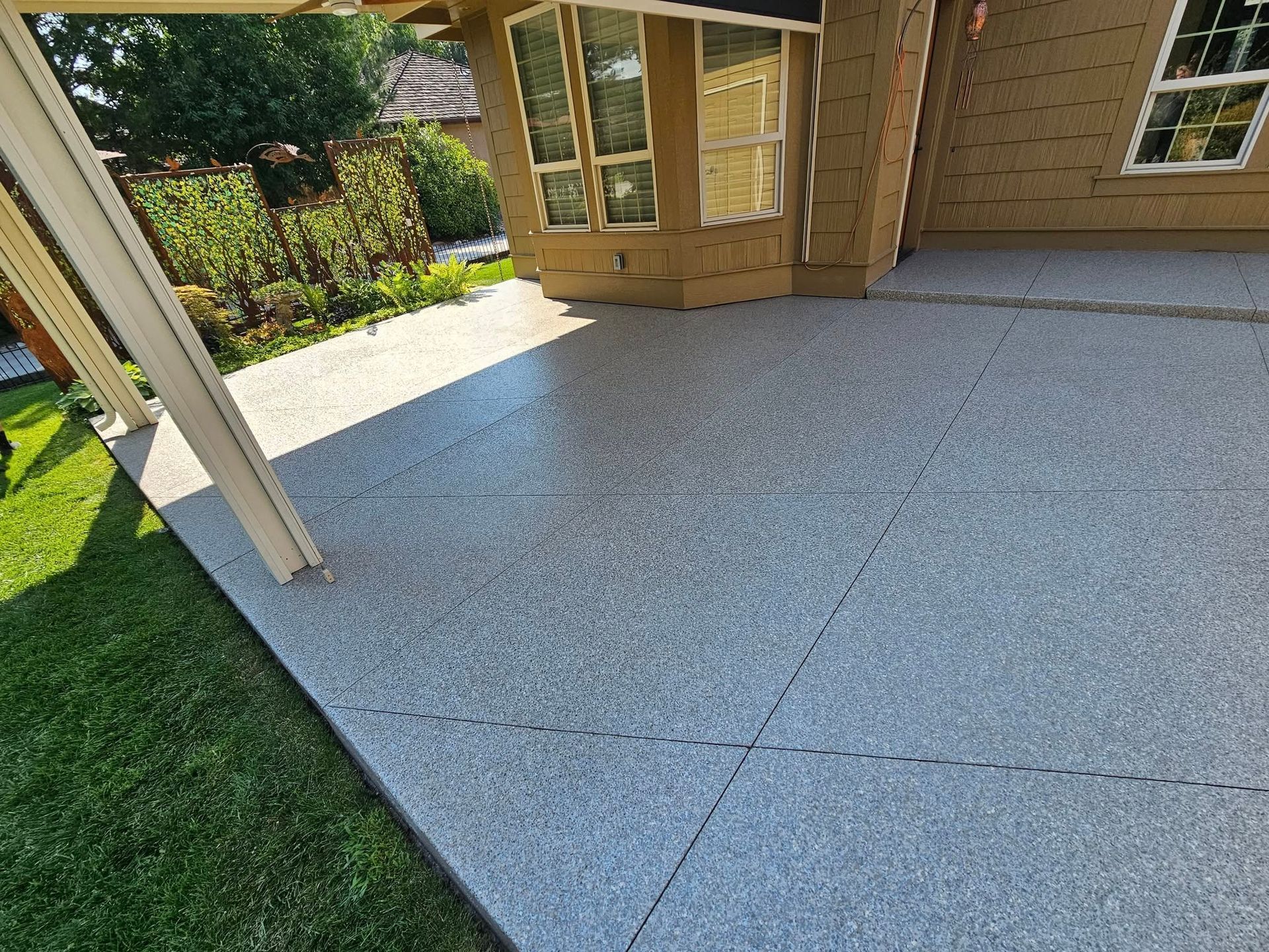 Back patio with light gray paving and wooden house exterior beside a green lawn