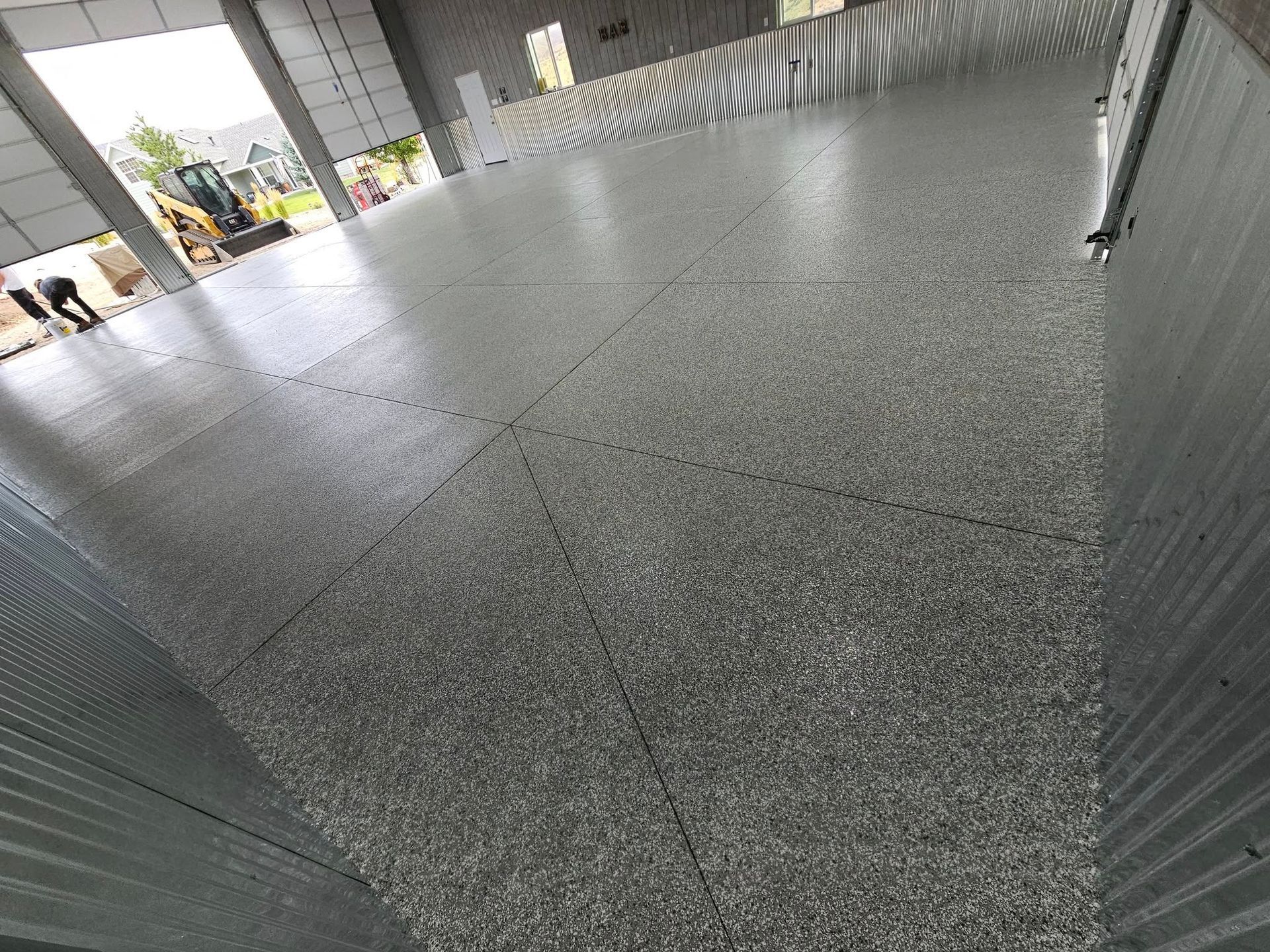 Empty tiled walkway under a covered structure, with a view of the outdoors at left and fencing at right.