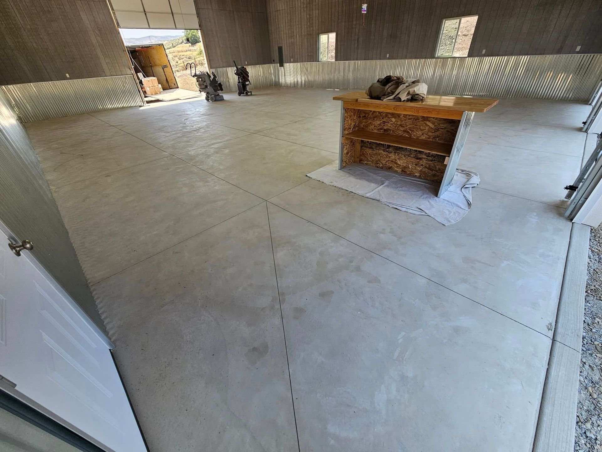 Empty warehouse interior with concrete floor, unfinished walls, and a wooden workbench in the center