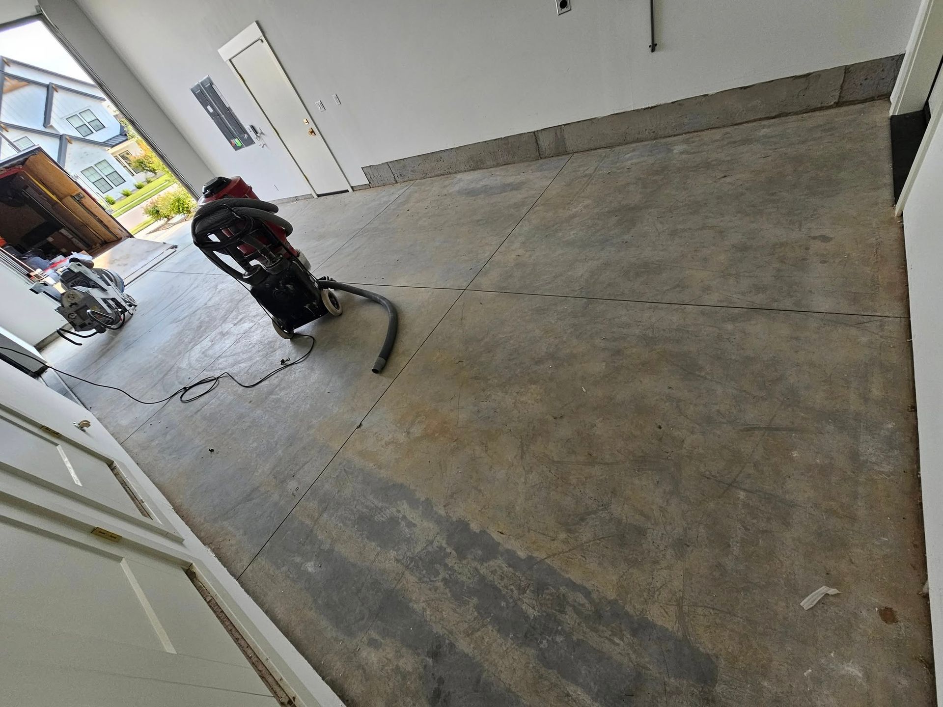 Person using a floor grinder on a concrete garage floor inside an open workshop