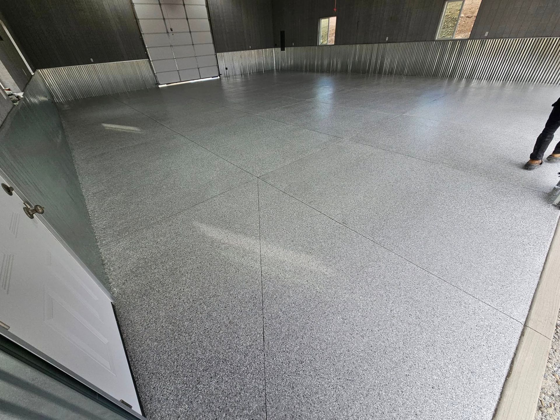 Empty indoor floor area with gray speckled flooring and a person’s legs at the right edge