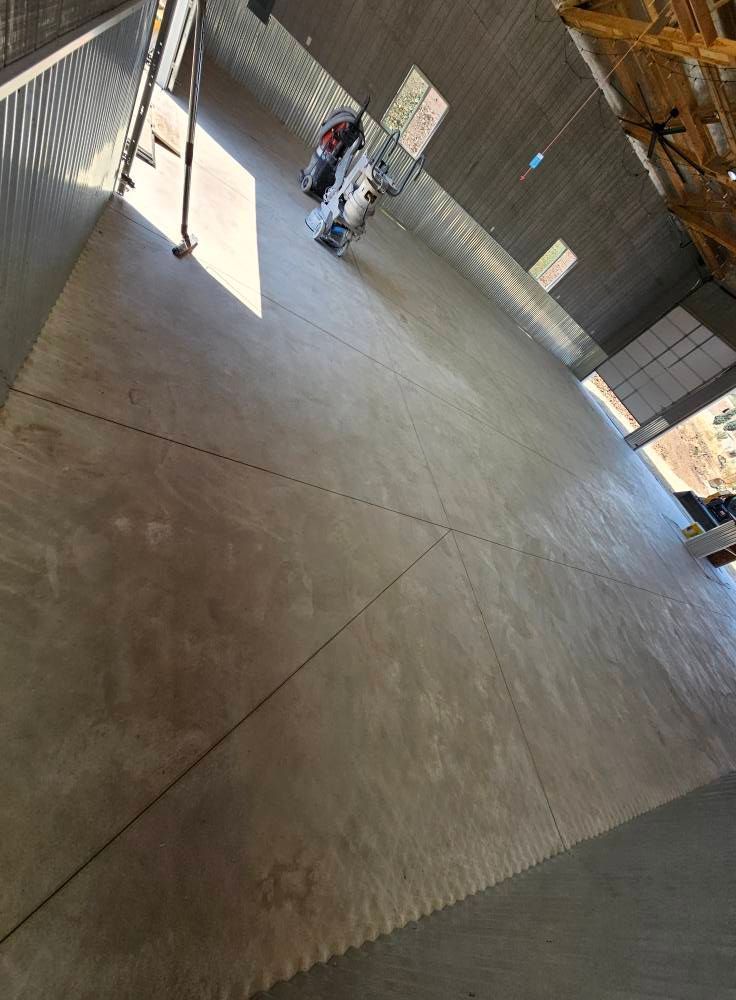 Empty concrete warehouse with a small vehicle near a sunlit entrance and stacked materials on the right.
