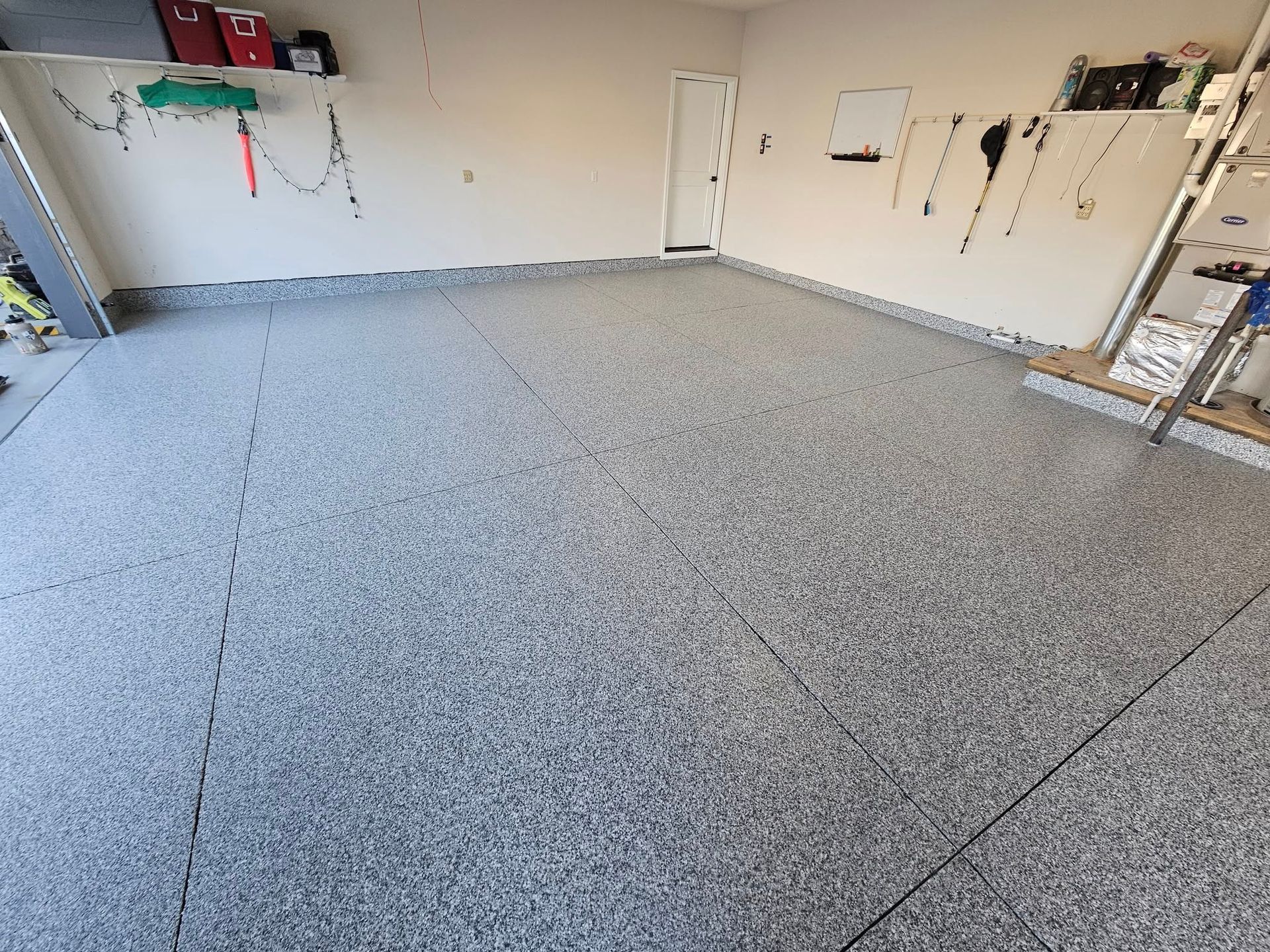 Empty garage with gray speckled floor and white walls, tools and shelving along the sides.