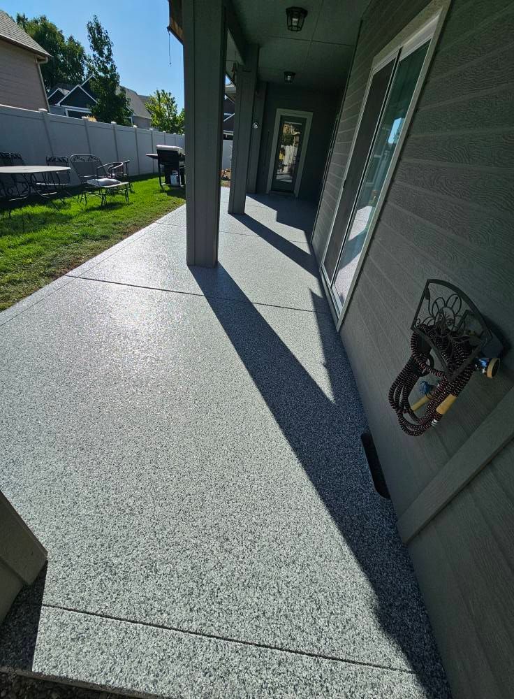 Covered concrete front porch with green siding, long shadows, and a stroller near the wall.