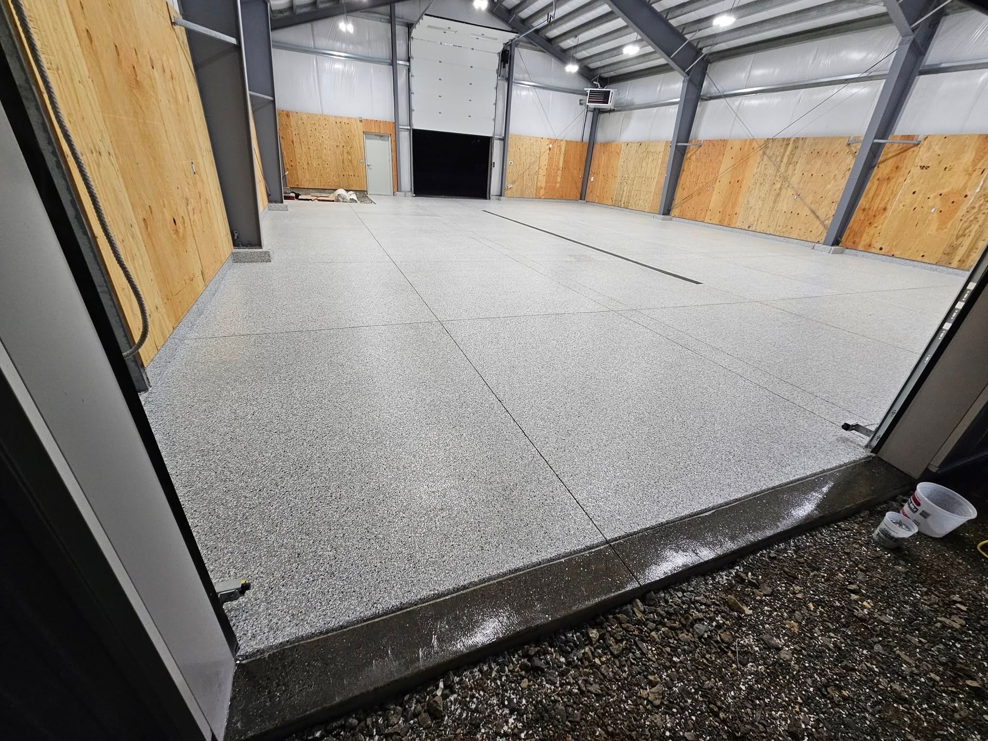 Empty warehouse interior with a large gray speckled floor and wood-paneled walls under metal beams