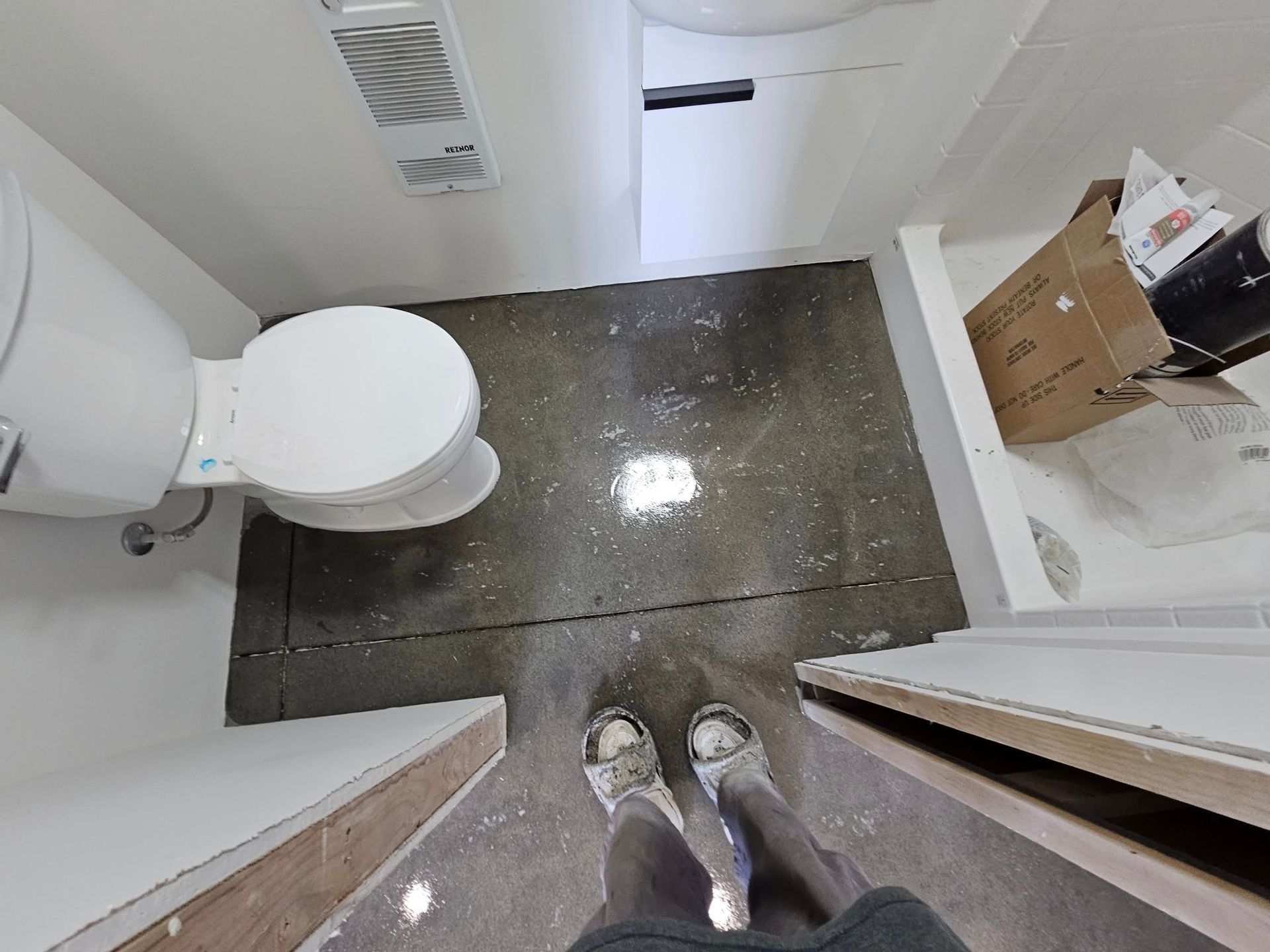 Small bathroom with white toilet, dark tile floor, and boxes on a shelf, viewed from the doorway.