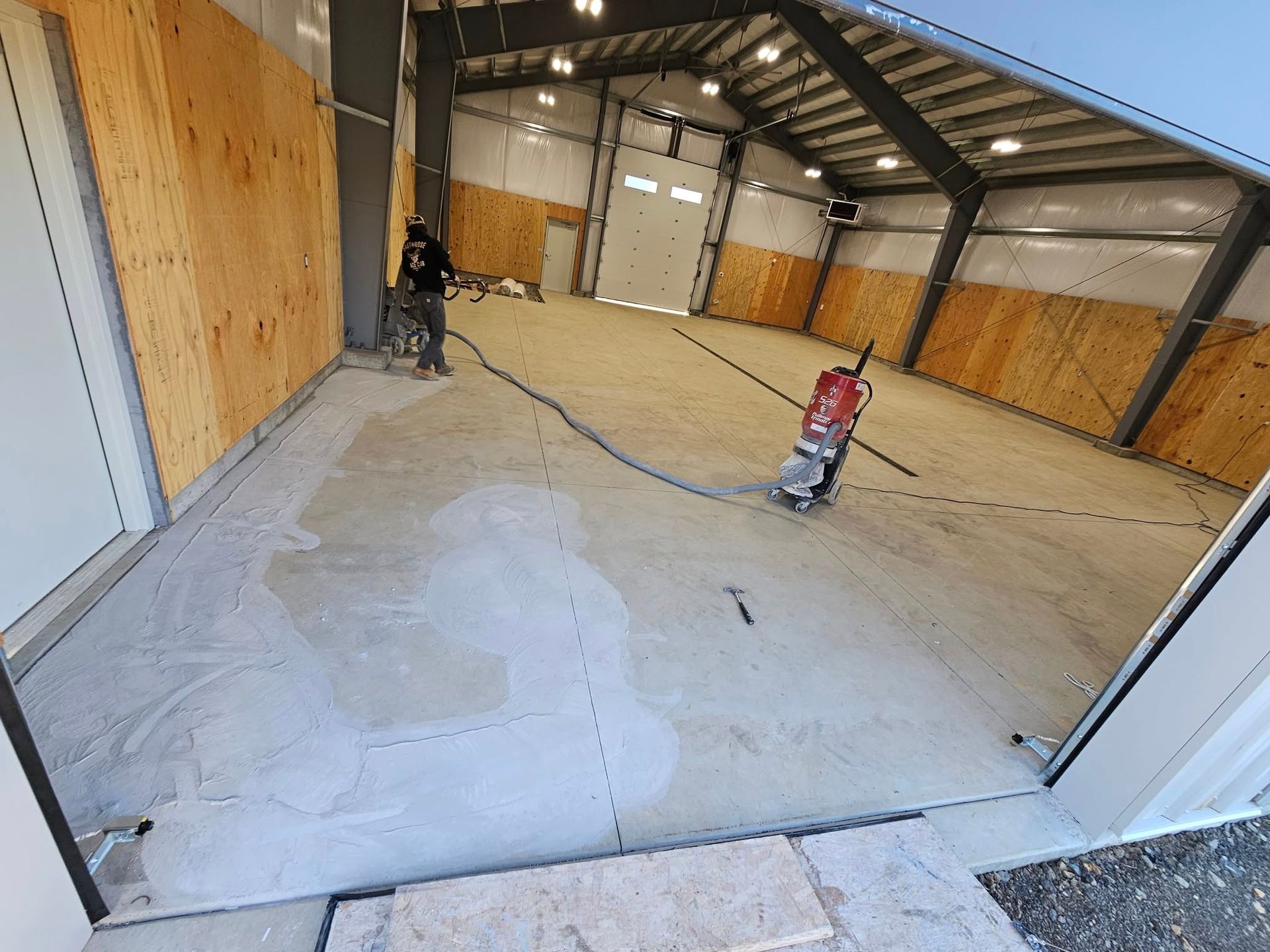 Empty warehouse interior with concrete floor being polished by a red floor grinder.