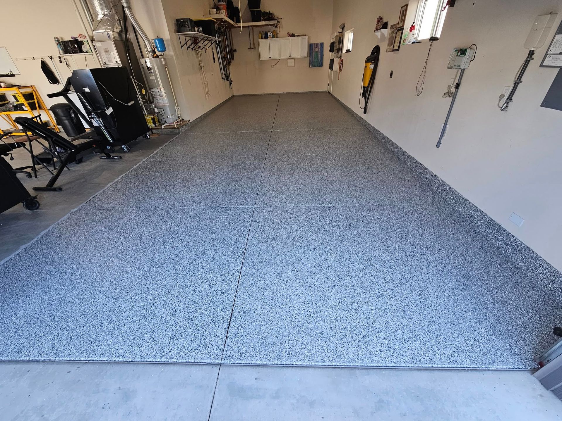 Empty garage with gray speckled epoxy floor and wall-mounted tools along the sides