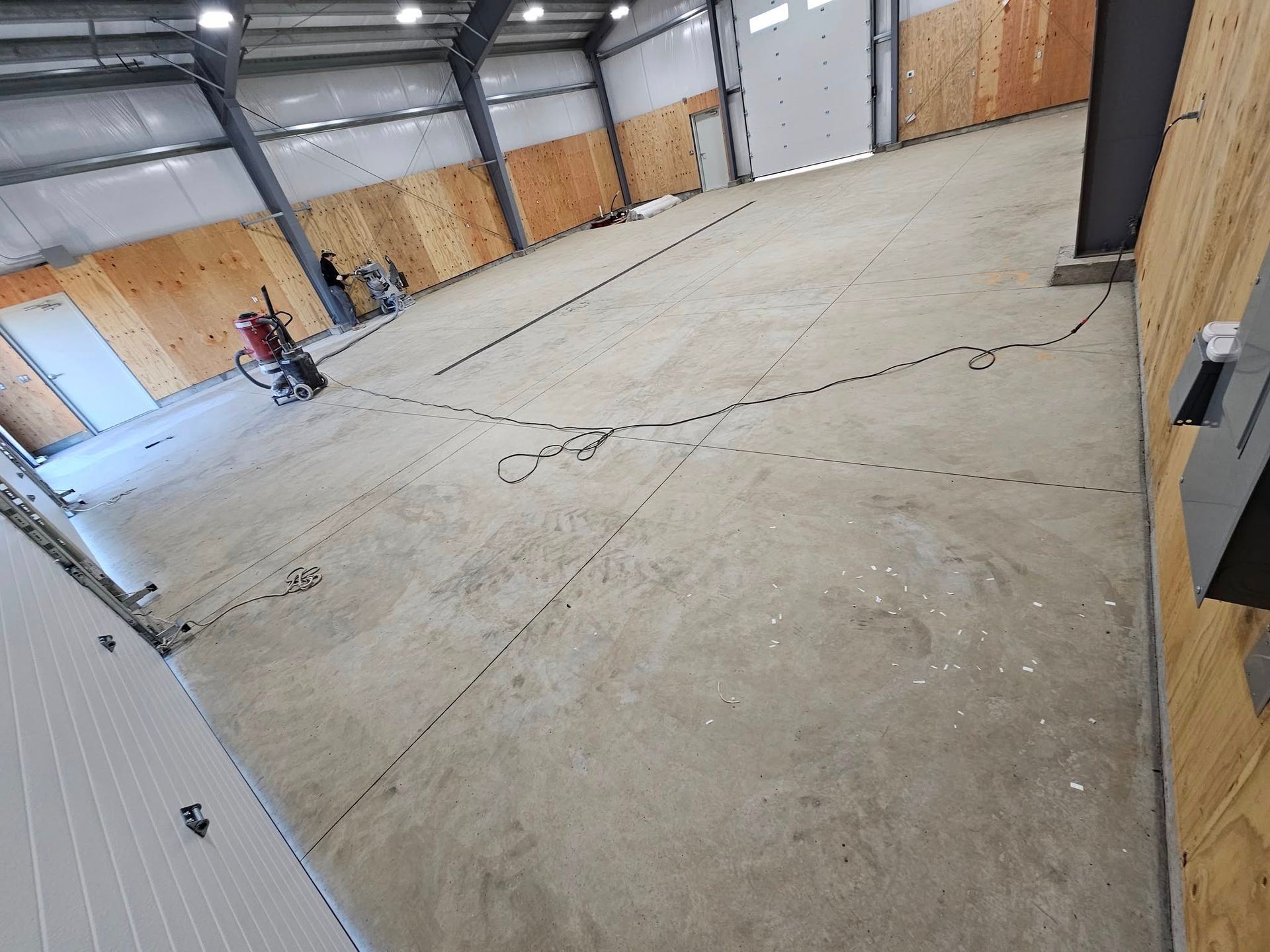 Empty industrial warehouse with concrete floor, wood-paneled walls, and overhead lights.