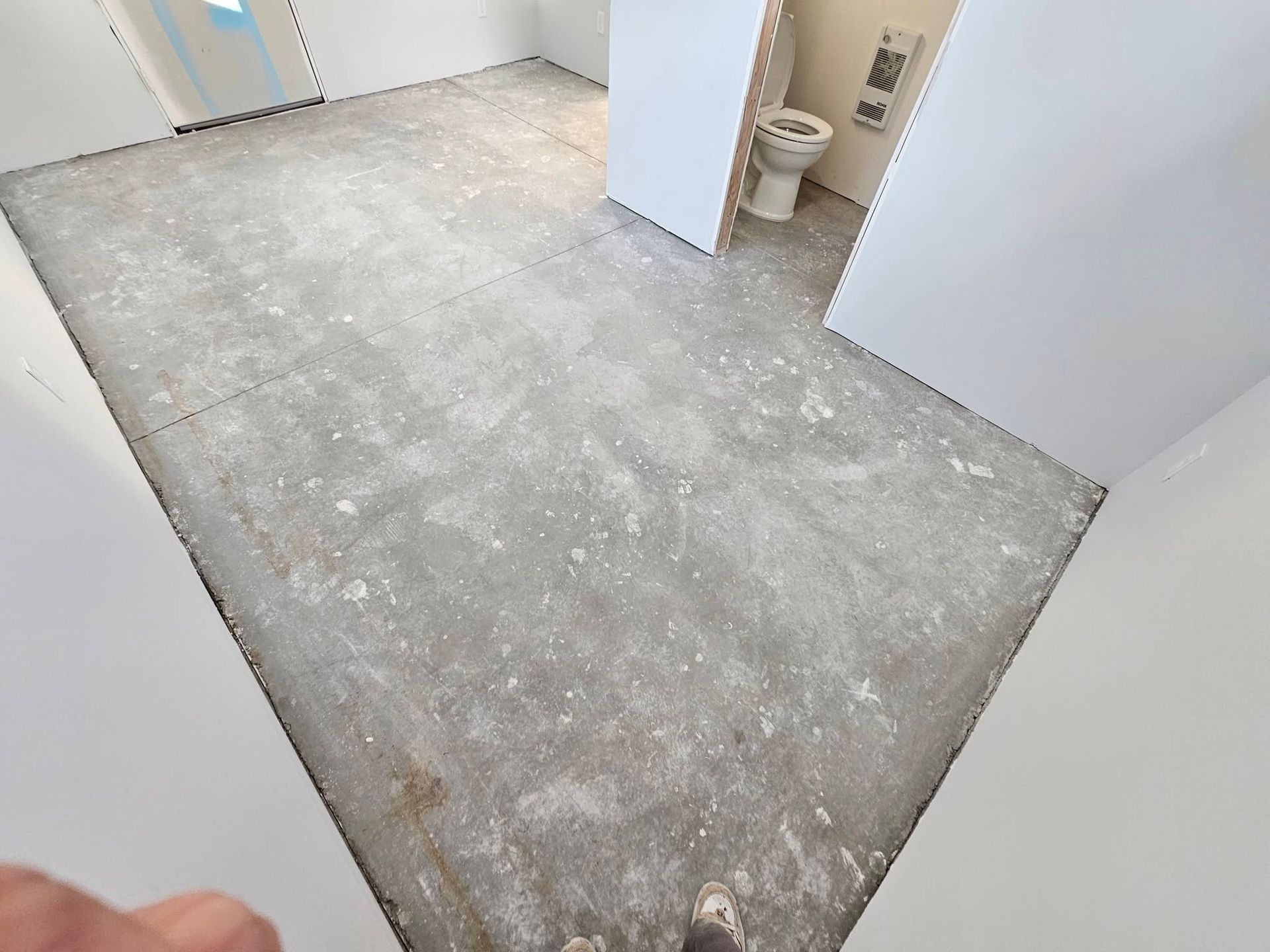 Bare concrete room under renovation with white walls and a toilet visible in the corner