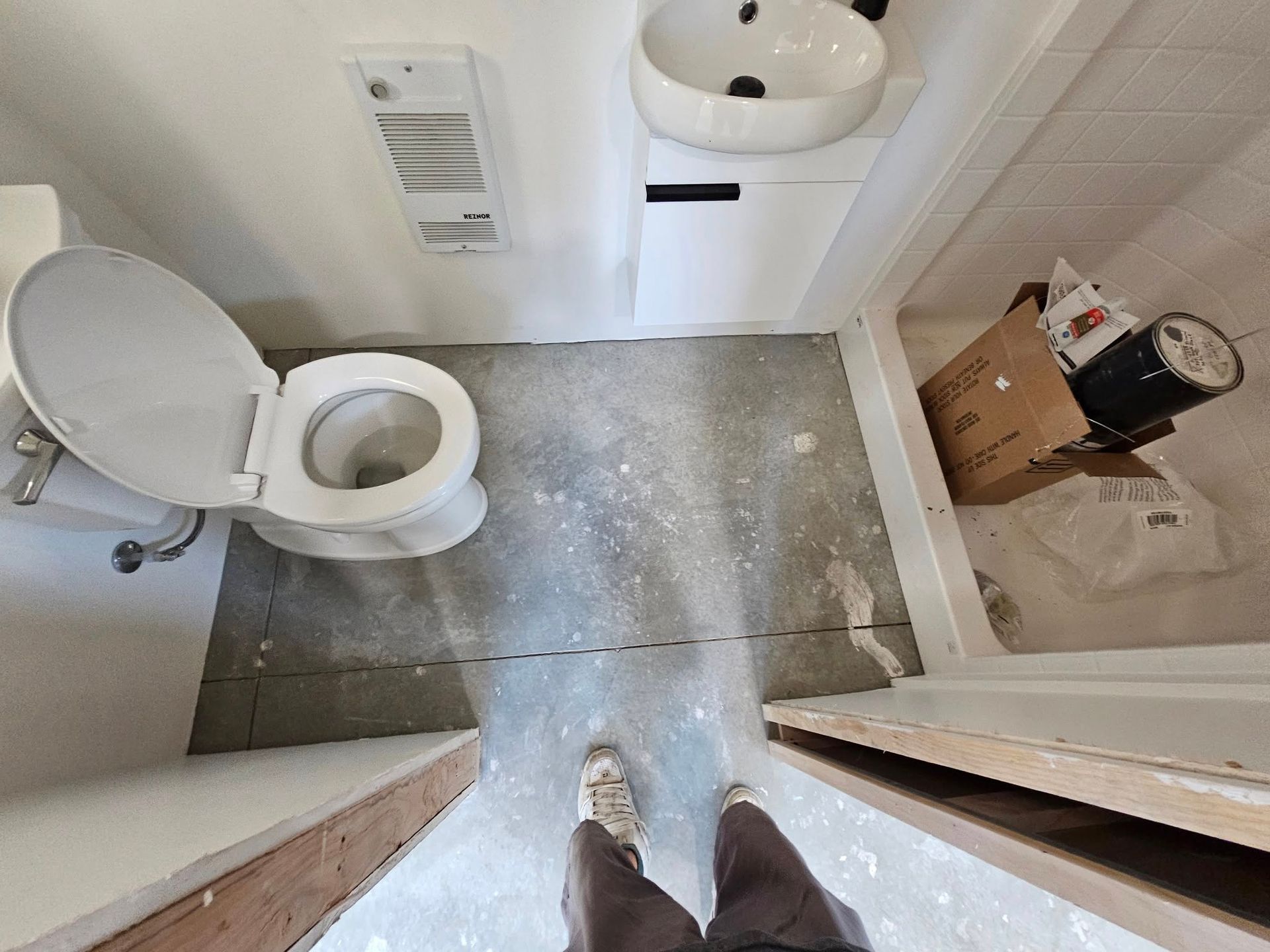 Small bathroom under renovation with toilet, sink, tile floor, and cardboard boxes on the right.