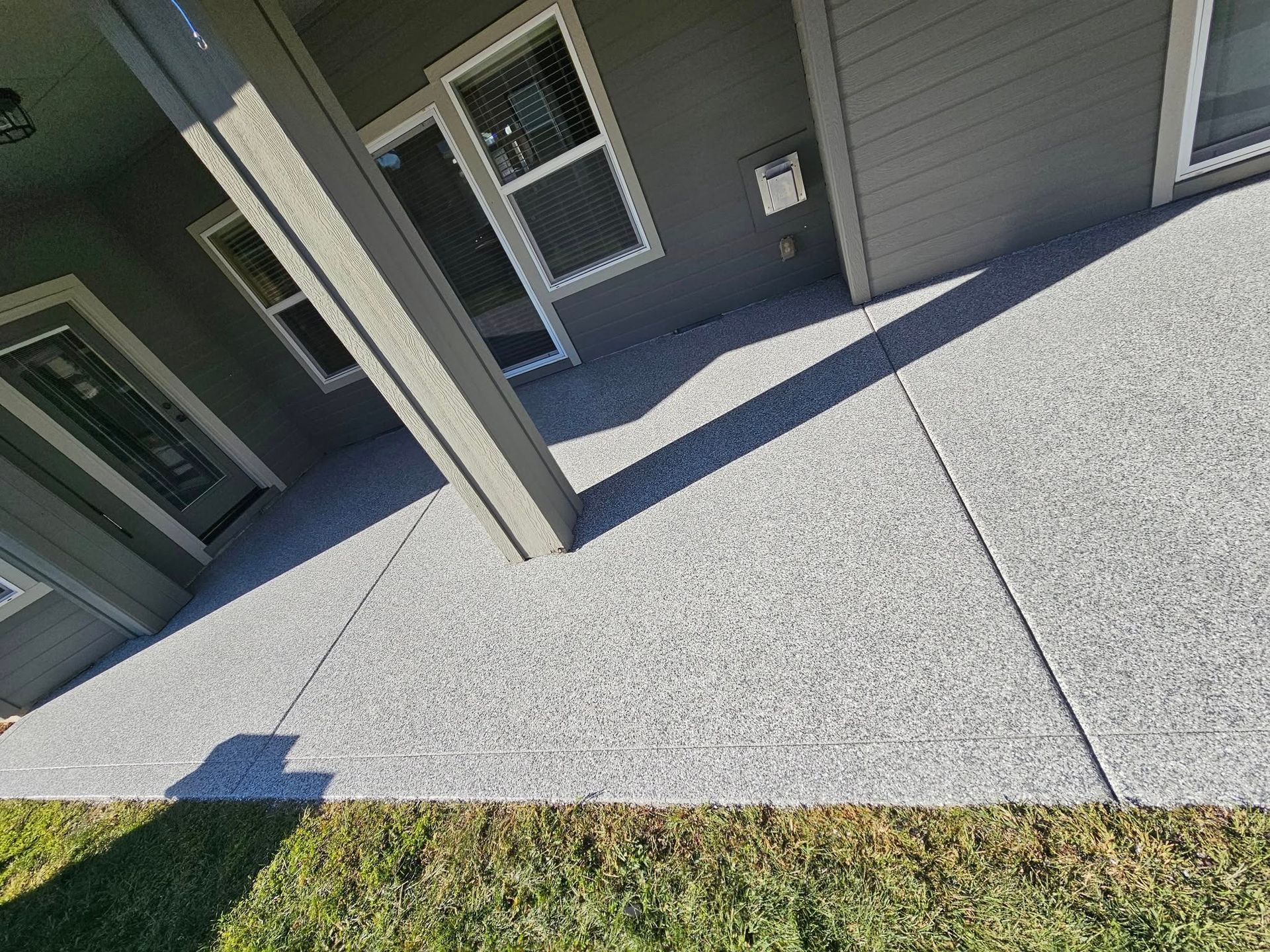 Covered apartment patio with concrete floor, gray siding, white columns, and small windows.