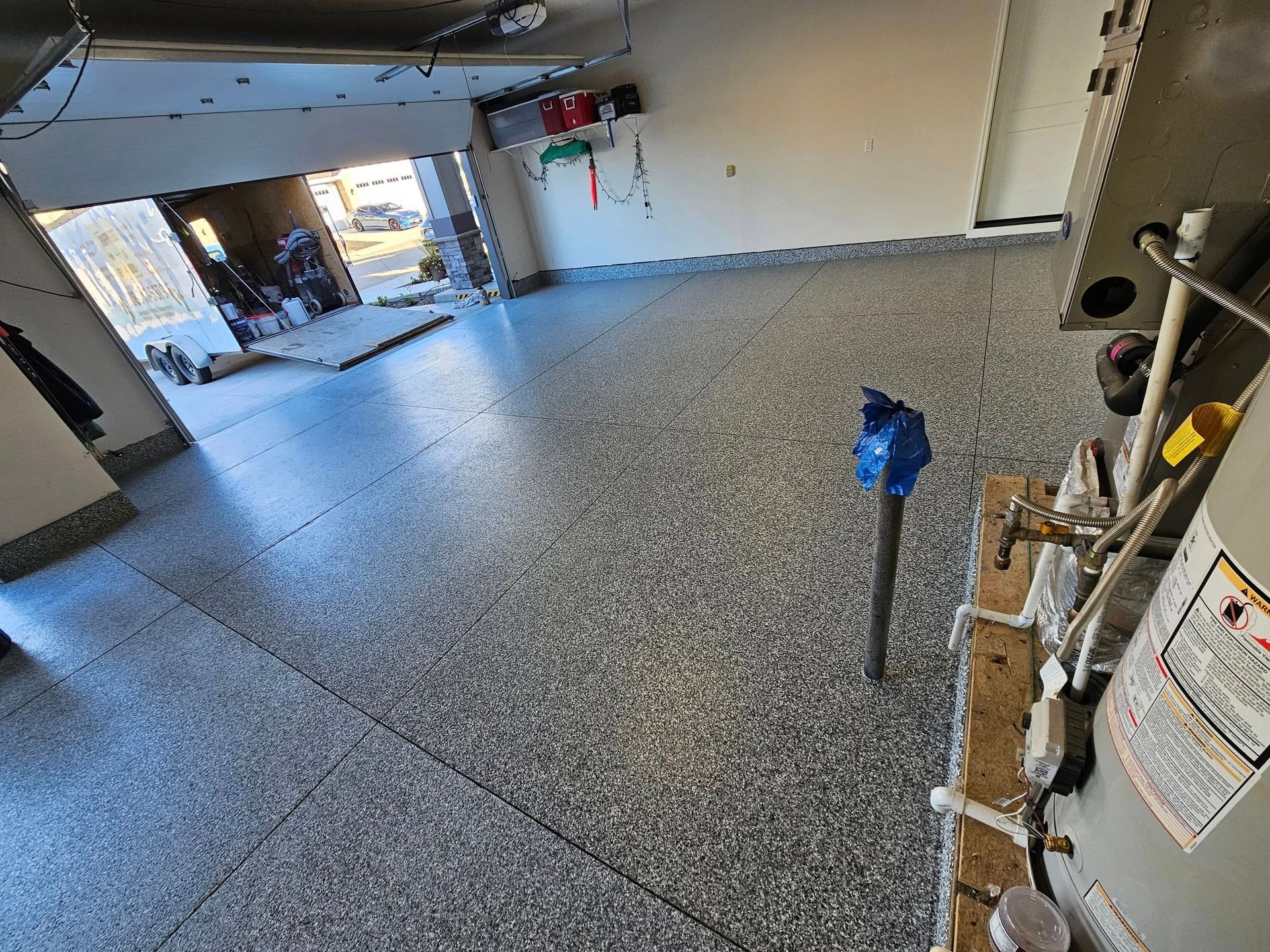 Spacious garage floor coated in gray epoxy, with a blue pipe and water heater on the right.