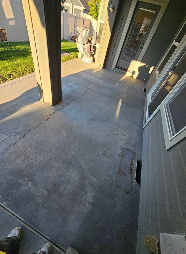 Covered concrete patio beside a gray house, with sunlit columns and a sliding door.