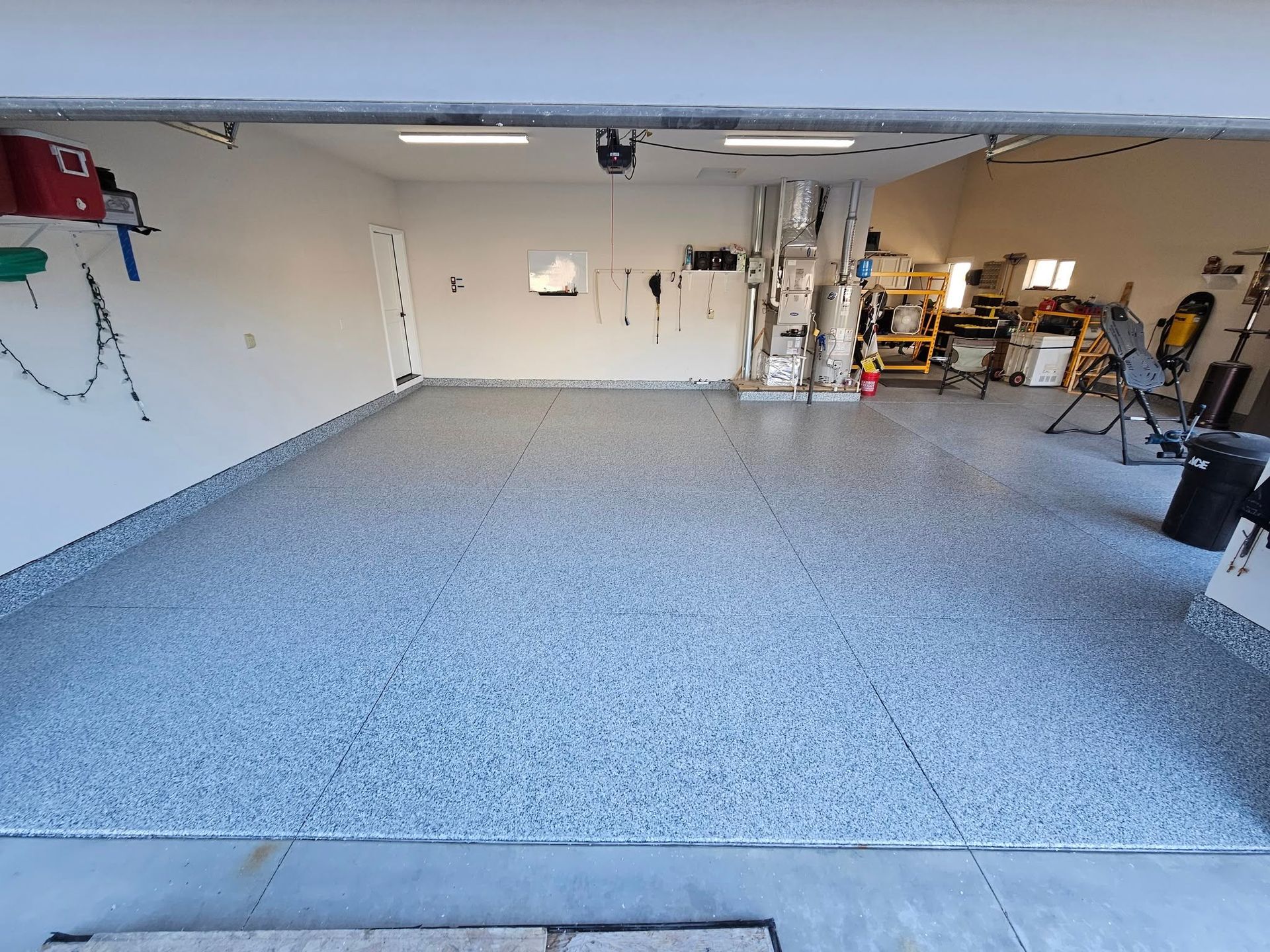Empty garage with gray epoxy floor, white walls, and shelves and tools along the right side.