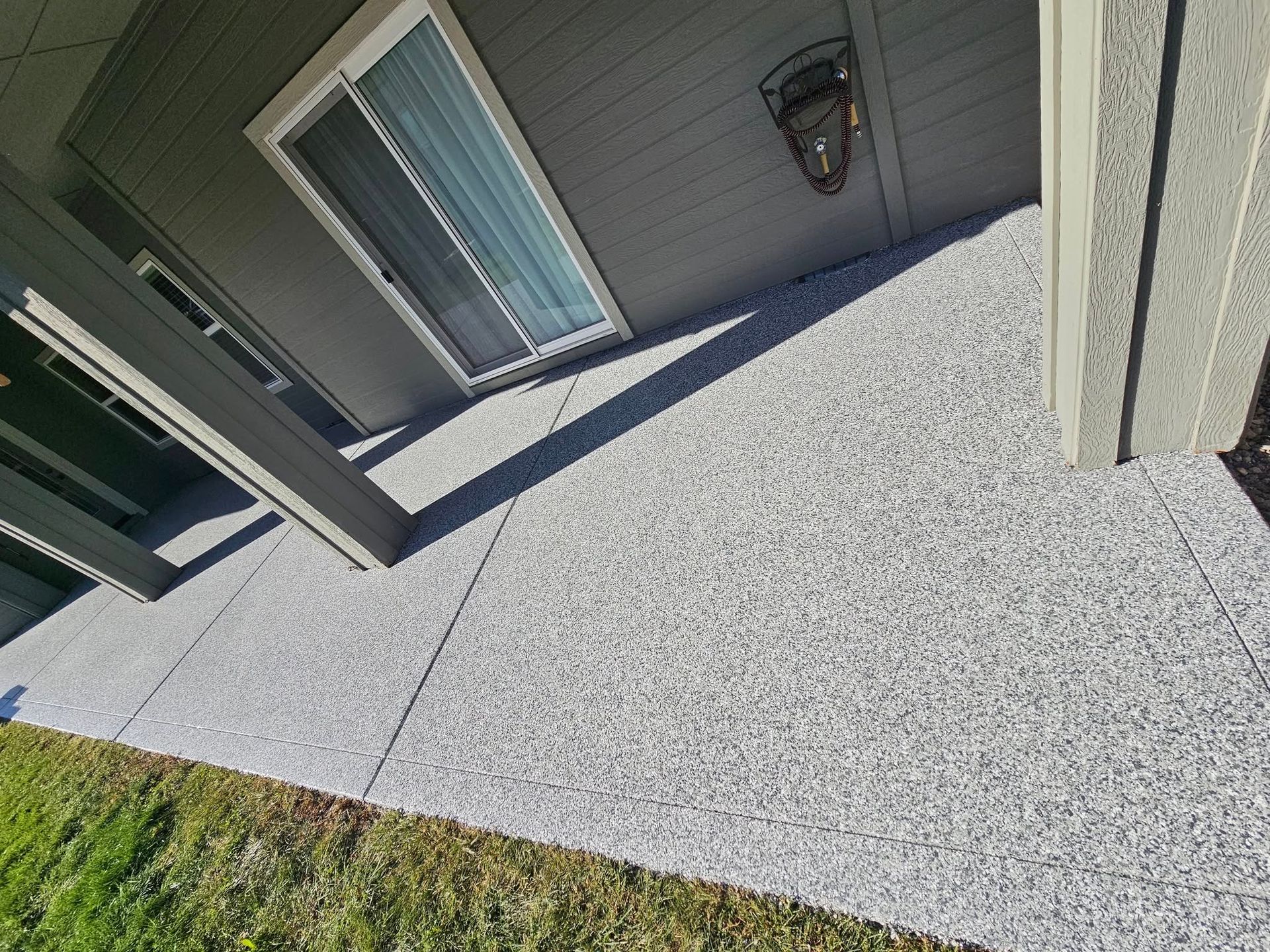 Angled view of a house patio with gray concrete, sliding glass door, and a wall lantern.