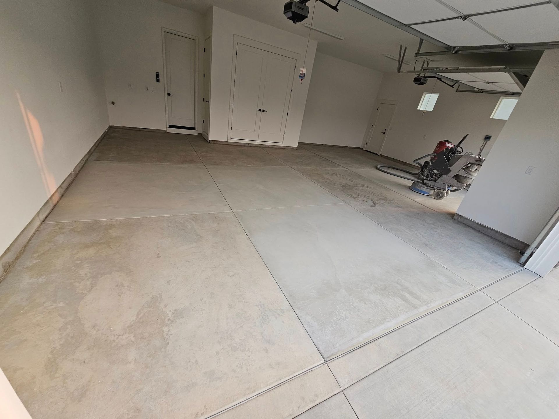 Empty garage with a concrete floor, white walls, and a lawn mower near the right wall