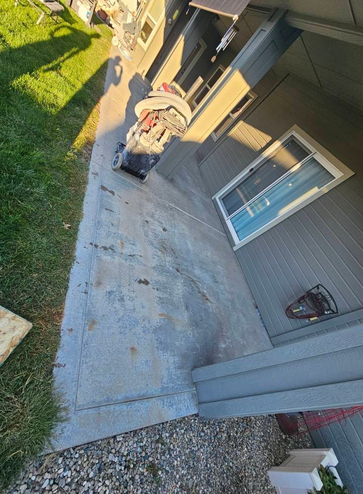 Concrete patio beside a house with a porch chair, window, and grassy yard