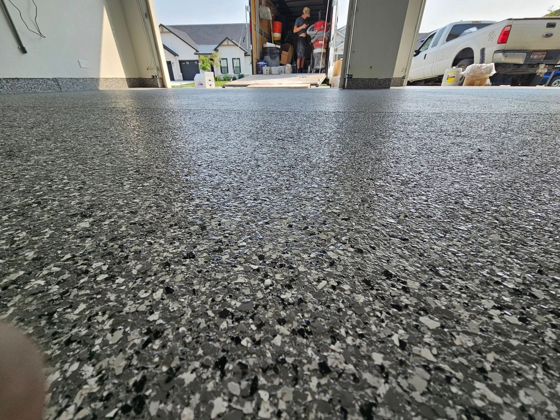 Low-angle view of a speckled driveway leading to an open garage with houses in the background