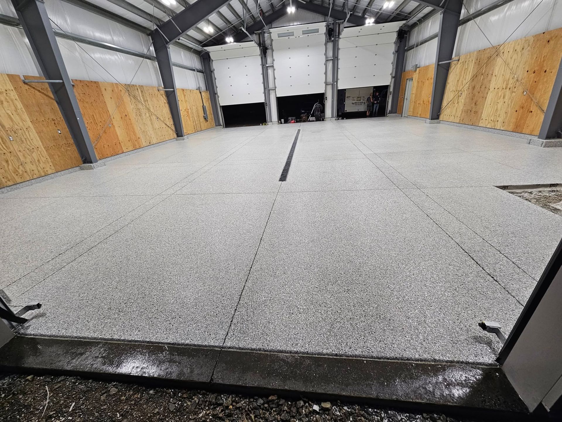 Empty indoor warehouse with a concrete floor, open bays, and plywood-covered walls and ceiling beams