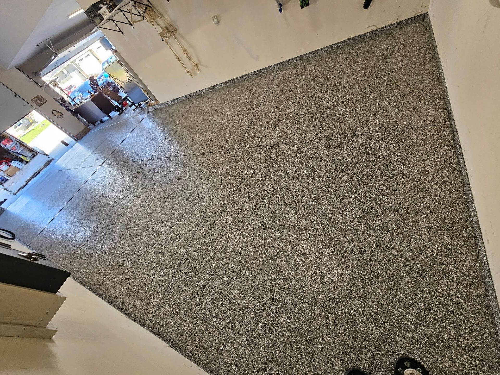 Tilted view of a school hallway with gray speckled floor, white walls, and a distant doorway with people.