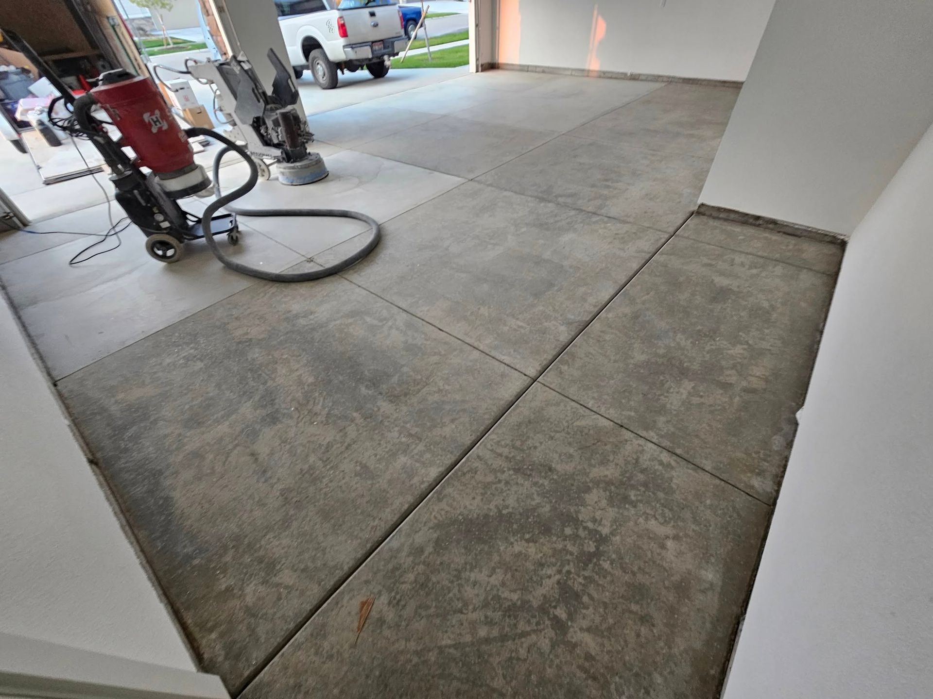 Concrete driveway inside a garage, with a vacuum cleaner and a bicycle near the open entrance.