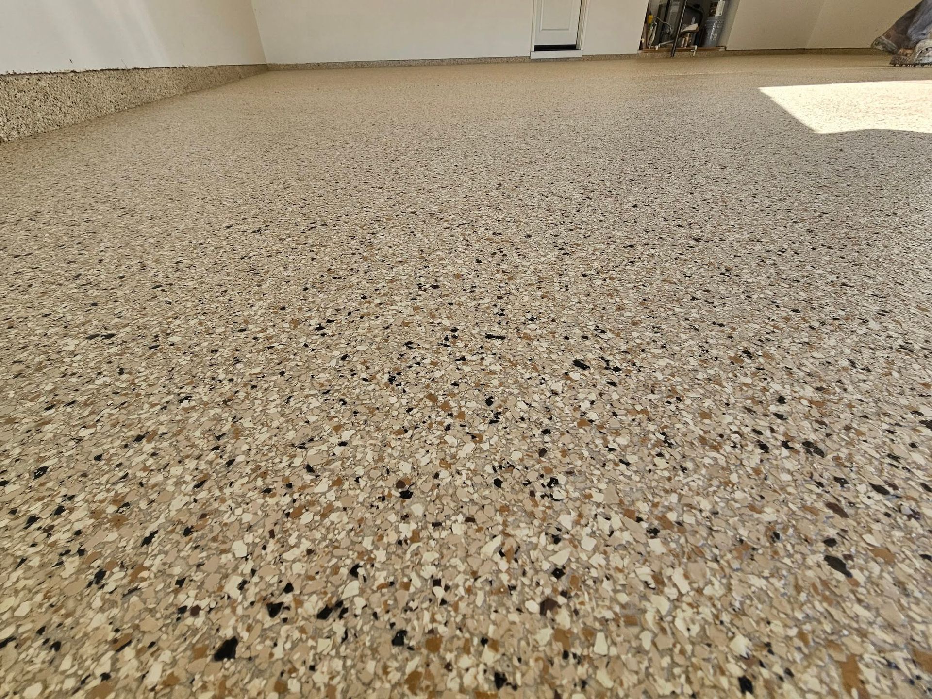 Empty speckled terrazzo floor in a bright room with sunlight near the wall