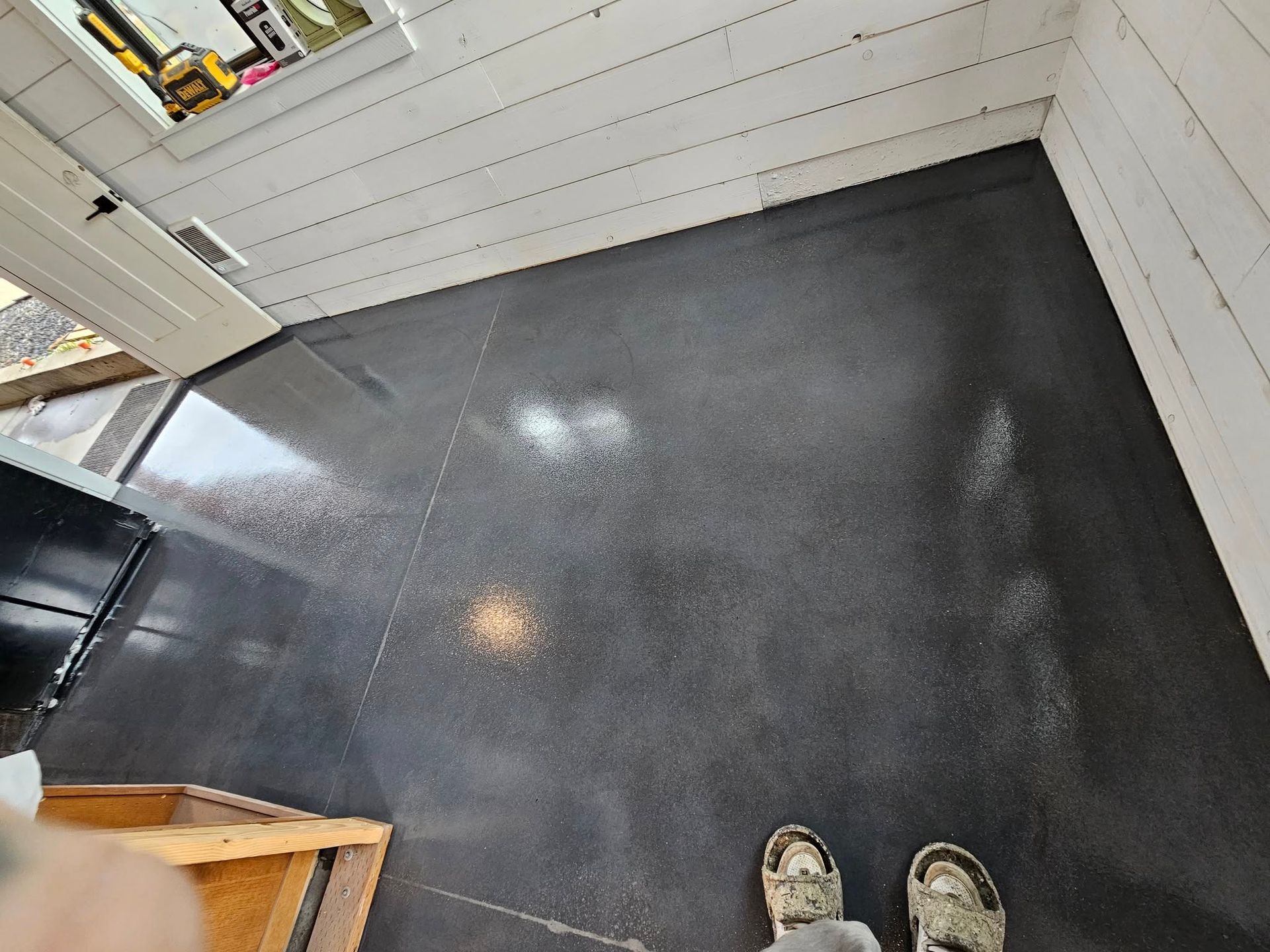 Small empty room with black floor, white walls, and shoes visible at the bottom edge