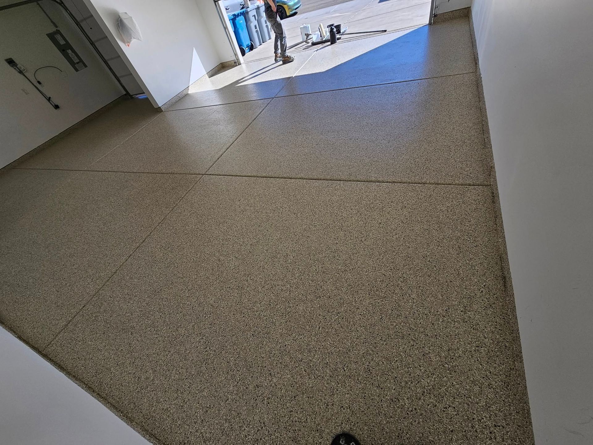 Indoor hallway with light-colored tiled floor leading toward a bright doorway.