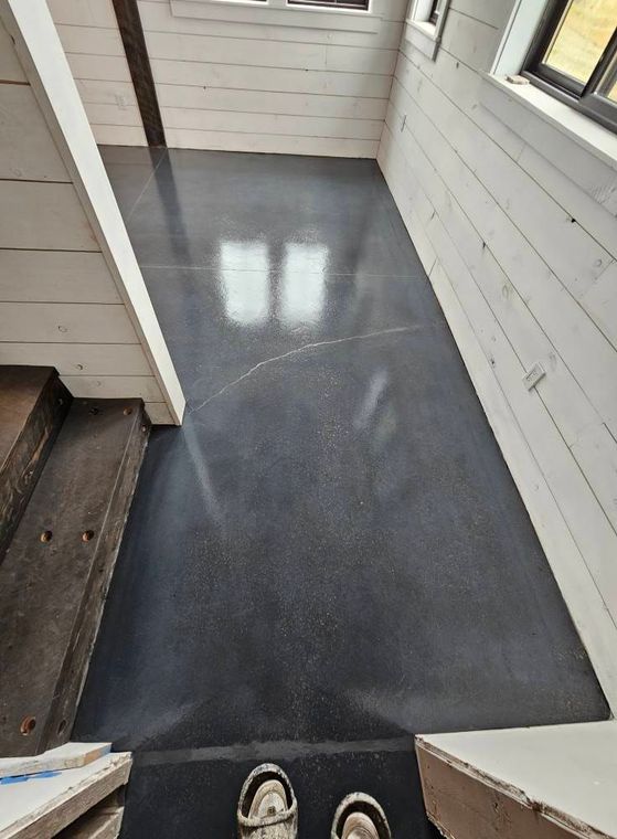 Narrow porch walkway with gray floor, white siding, stairs on the left, and windows on the right.