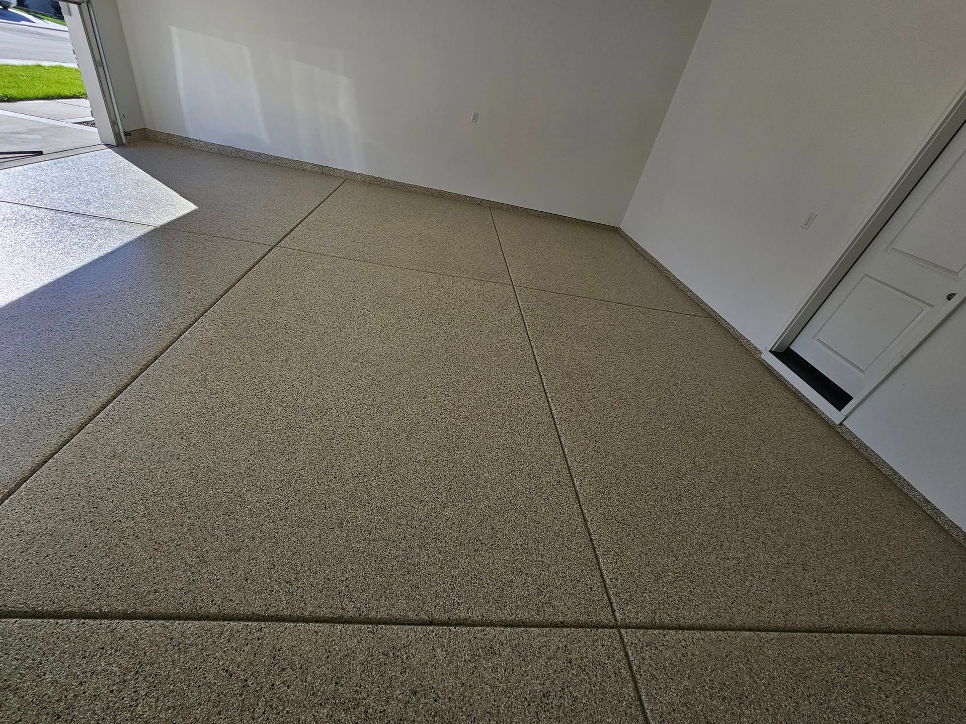 Concrete garage floor with expansion joints, viewed toward an open doorway and white walls