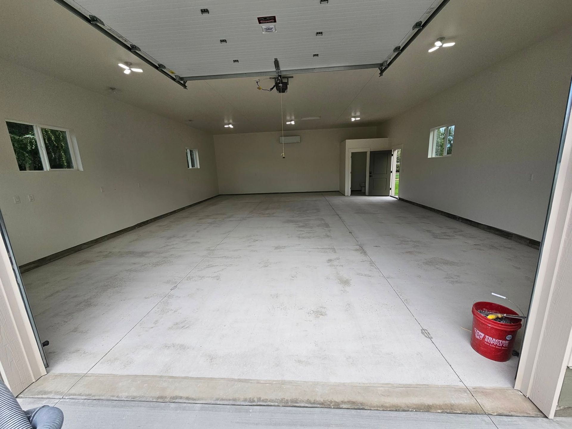Empty unfinished garage interior with concrete floor, beige walls, and a red bucket near the entrance