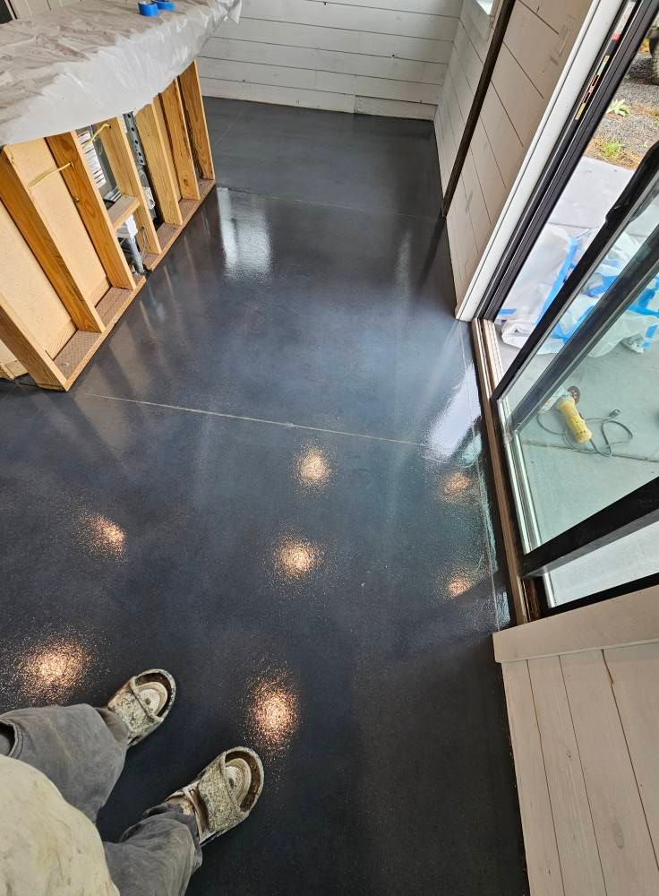 Small entryway with dark floor, staircase railing, glass door, and a person’s shoes at the bottom of the frame