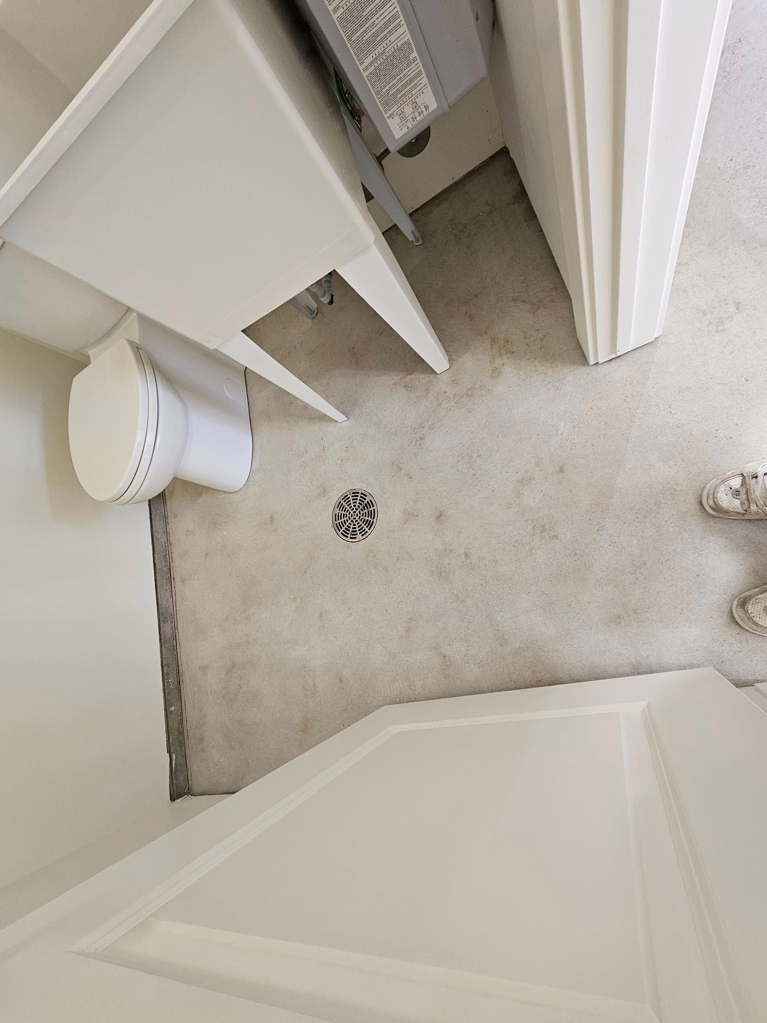 Small bathroom corner with shower door, white cabinetry, and a floor drain on light tile.