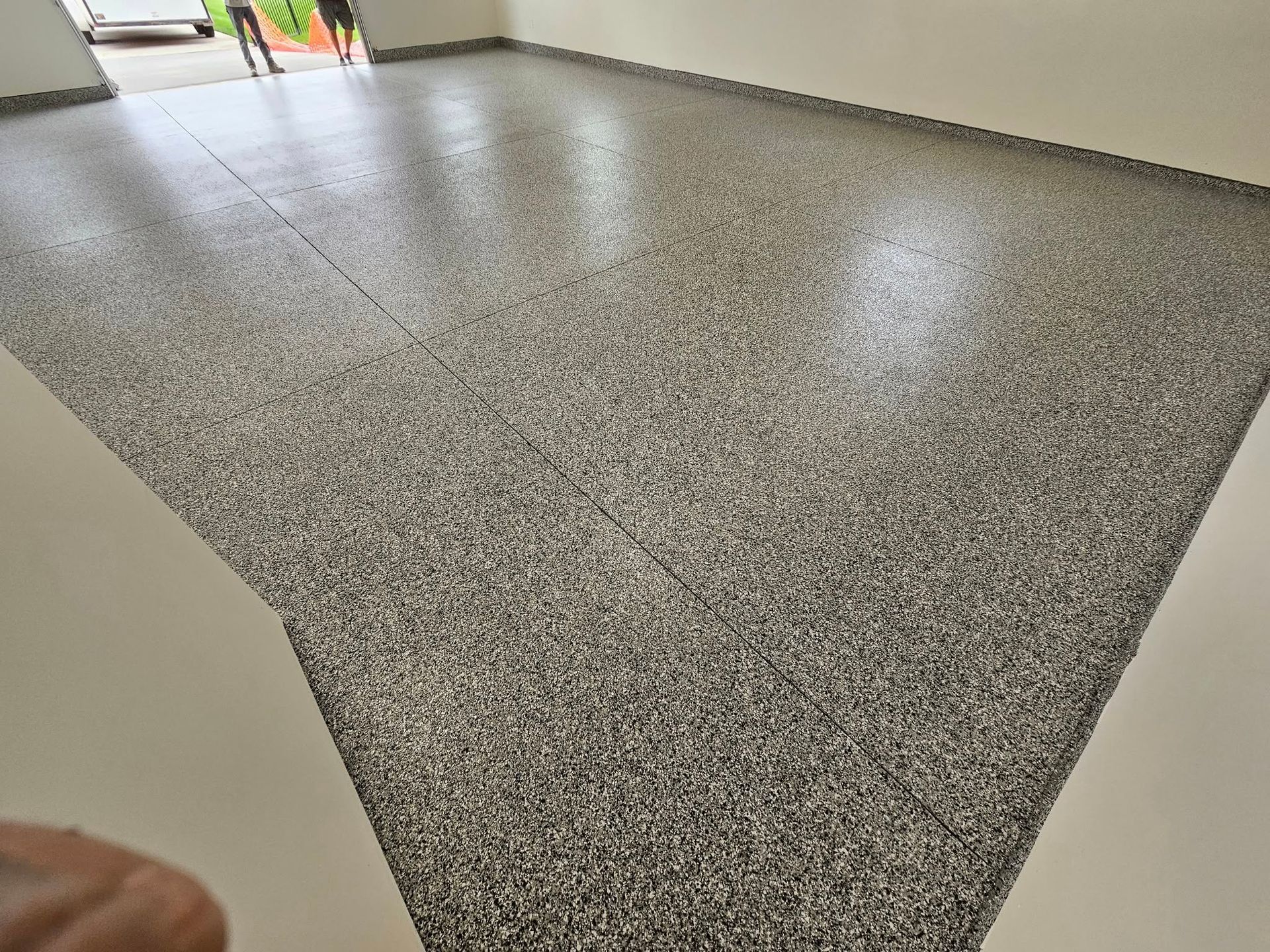 Empty speckled gray floor in a hallway with beige walls and bright reflections