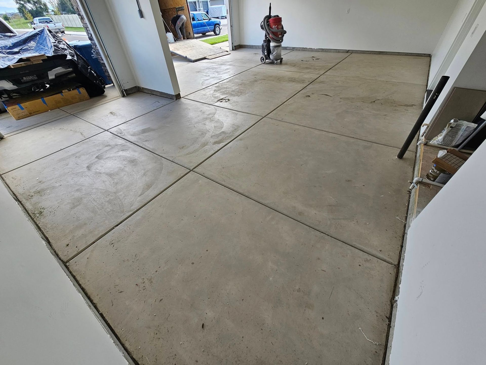 Concrete garage floor with expansion joints and a small robot vacuum near the open doorway.