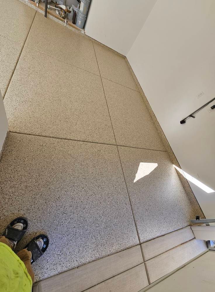 Hallway floor with speckled tiles, a person’s feet at bottom left, and sunlight on the right wall