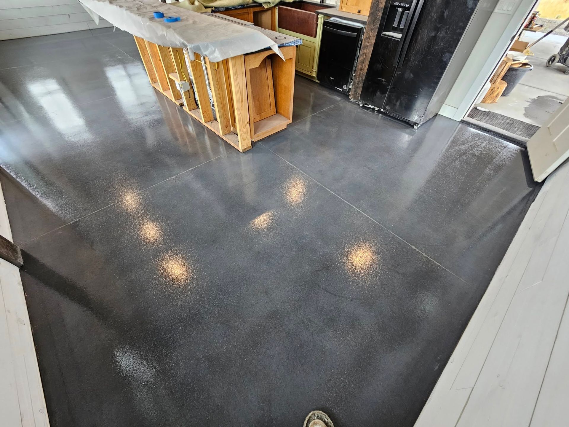 Modern kitchen with glossy dark floor, white island, and a wooden cabinet wrapped for renovation