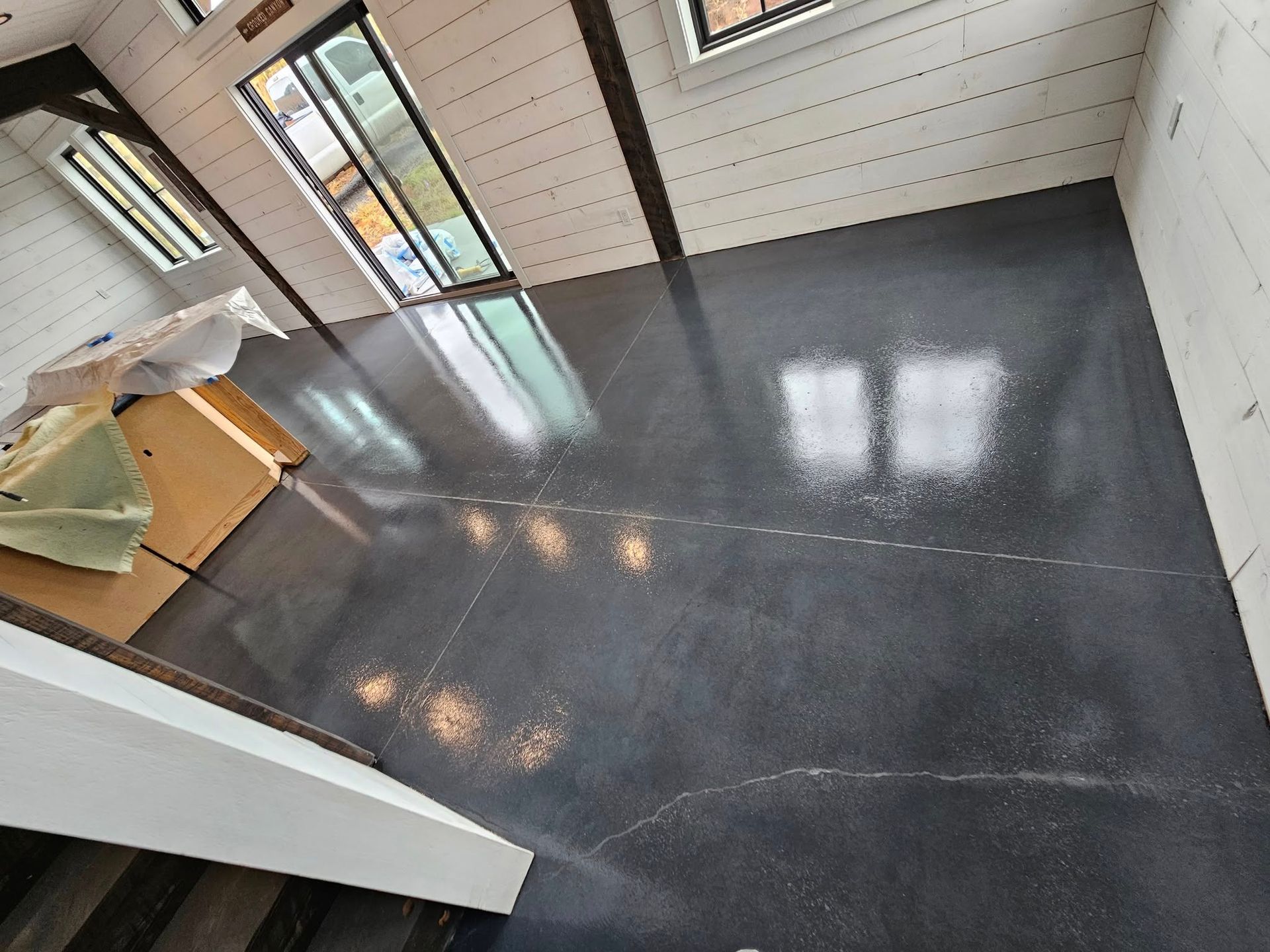 Empty modern room with dark tiled floor, white walls, and tall windows letting in natural light
