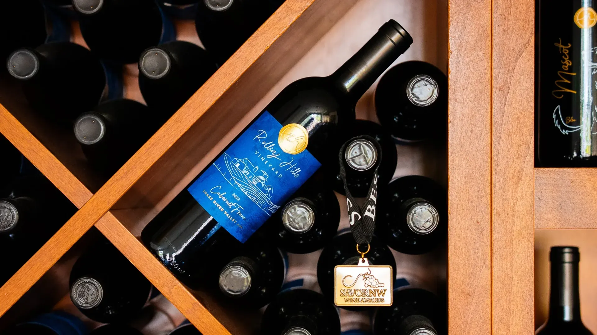 Wine bottles stored in a wooden rack, with one blue-labeled bottle prominently displayed.