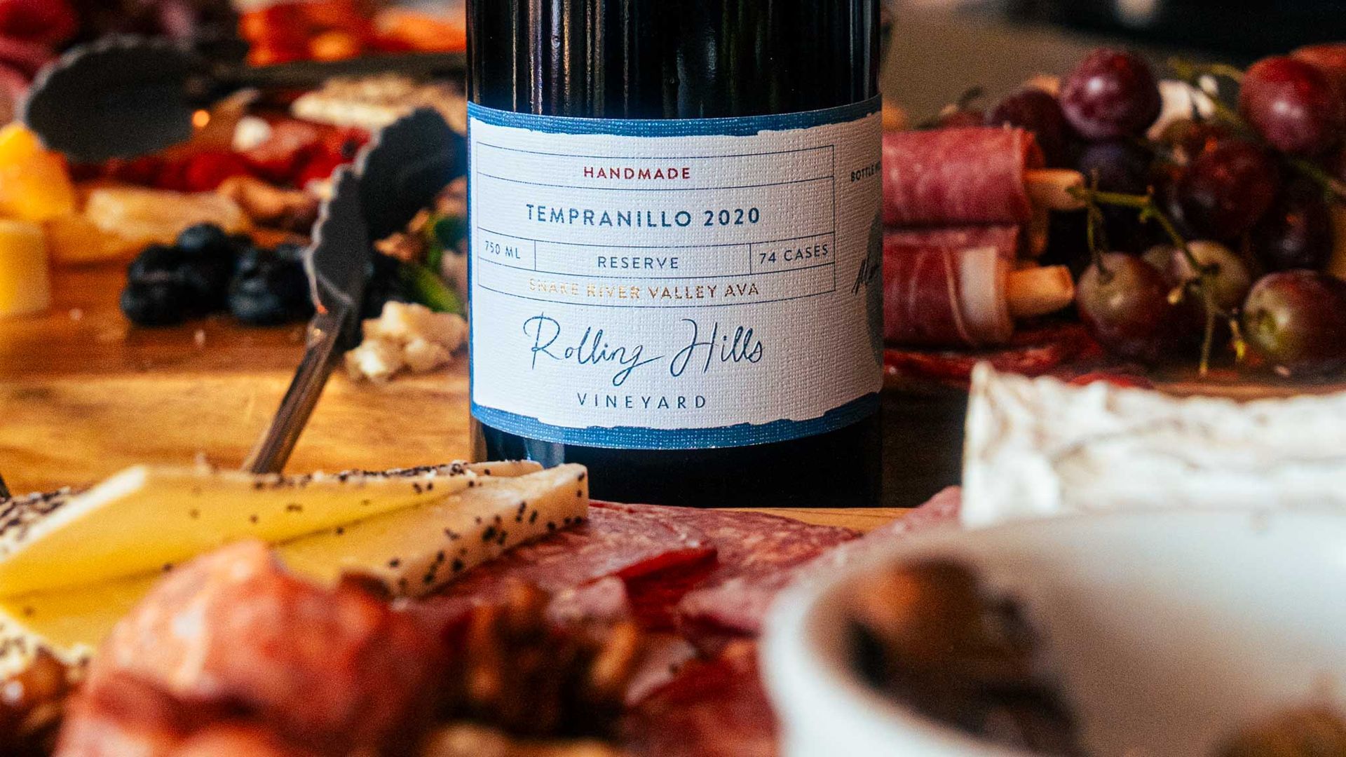 Wine bottle on a charcuterie board with cheese, grapes, and cured meats