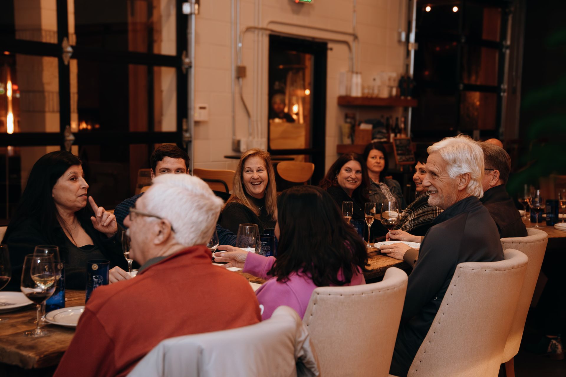 People seated around a dining table in a warmly lit restaurant, chatting and smiling.