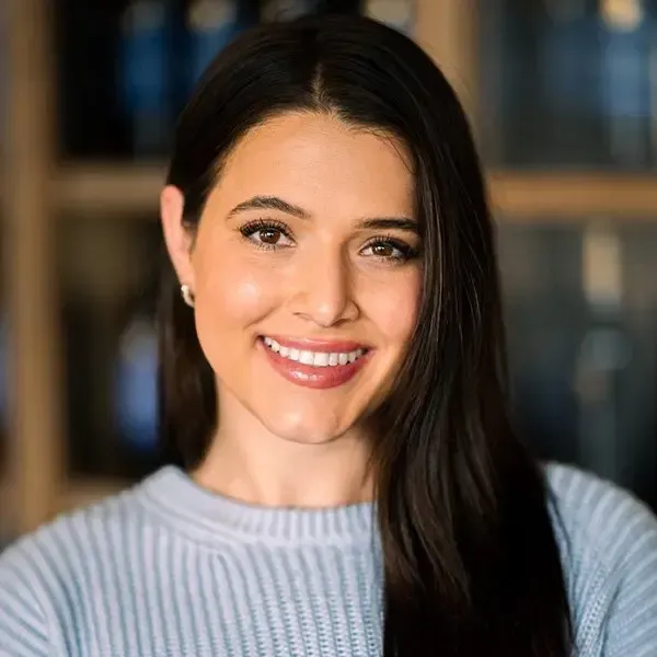 Woman with long dark hair, smiling, wearing a blue sweater.