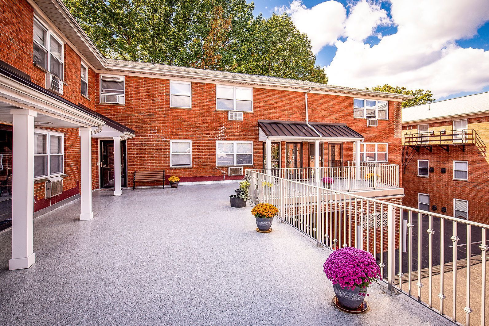 Exterior of a brick apartment building with a wide terrace, railing, and colorful potted flowers. Ready to make Joralemon your home? Contact us today to learn more about our pet-friendly 1, 2, and 3-bedroom apartments for rent in Belleville, NJ. We can’t wait to welcome you home!