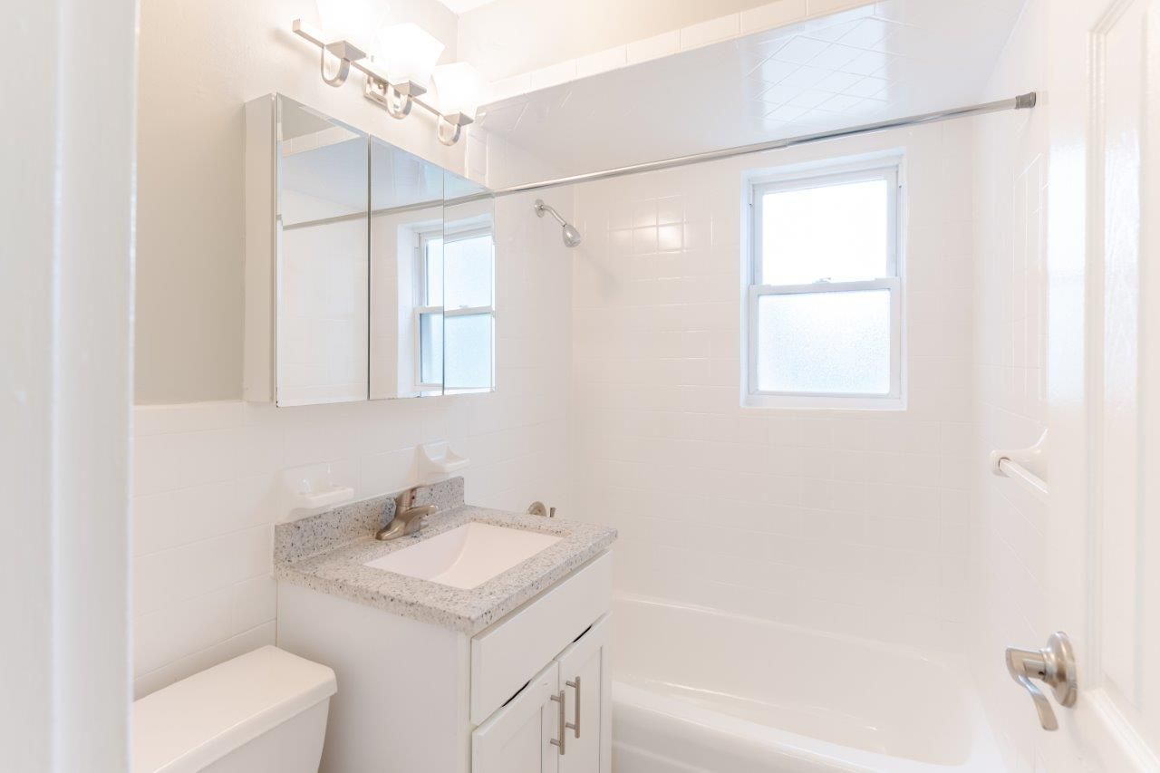 Bright white bathroom with vanity, mirror, sink, tub, and asmall window
