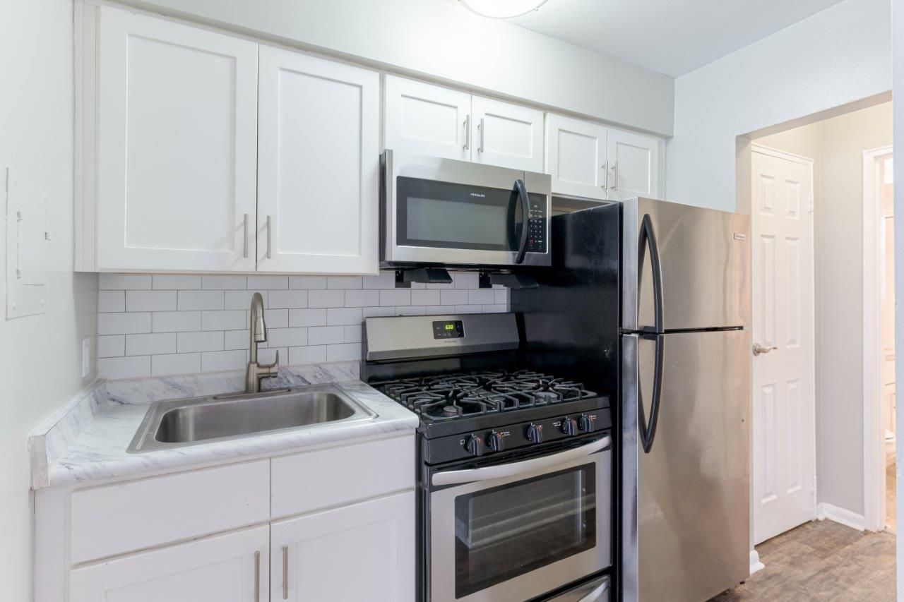 Bright white kitchen with stainless steel appliances, sink, microwave, stove, and refrigerator.