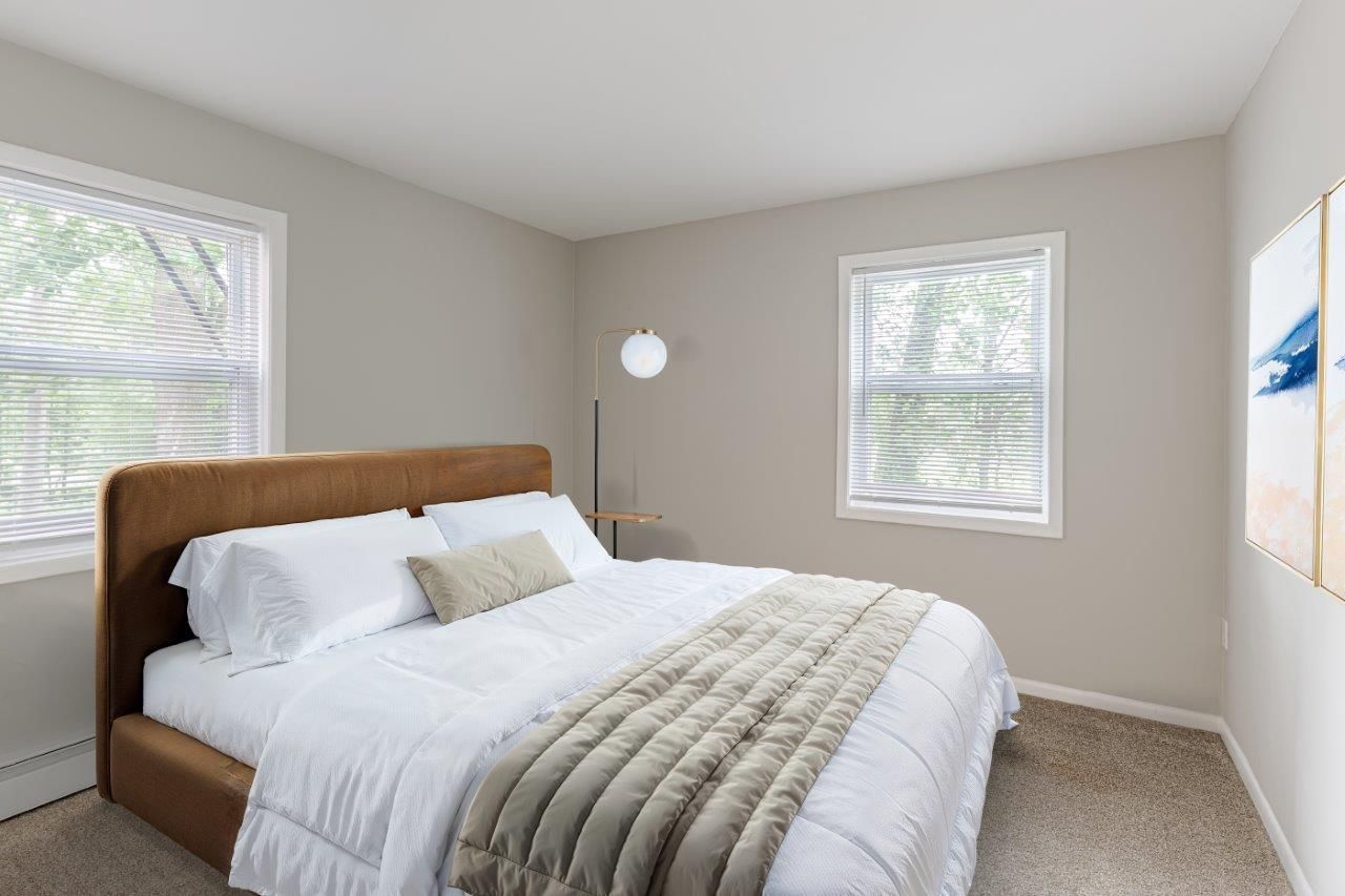 Bright bedroom with a wooden bed, white bedding, and two windows.