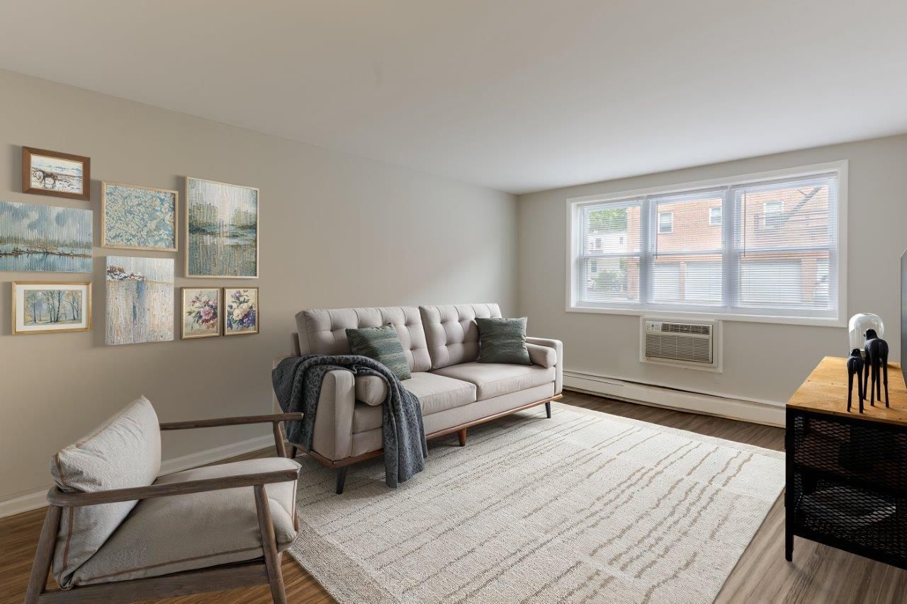 Modern living room with beige walls, gray sofa, white rug, gallery art, and a large window with blinds.