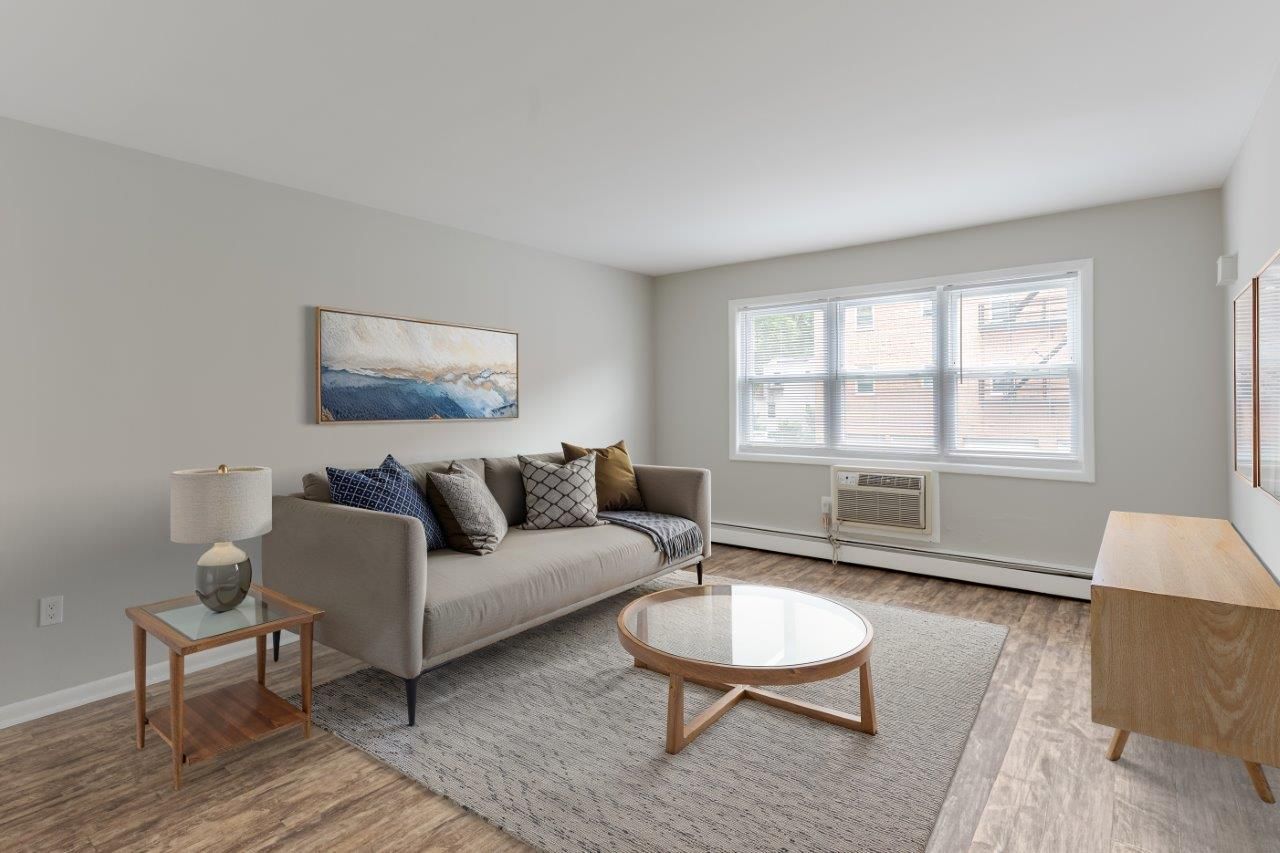 Bright living room with gray sofa, round coffee table, rug, wall art, and window seat beneath a large window