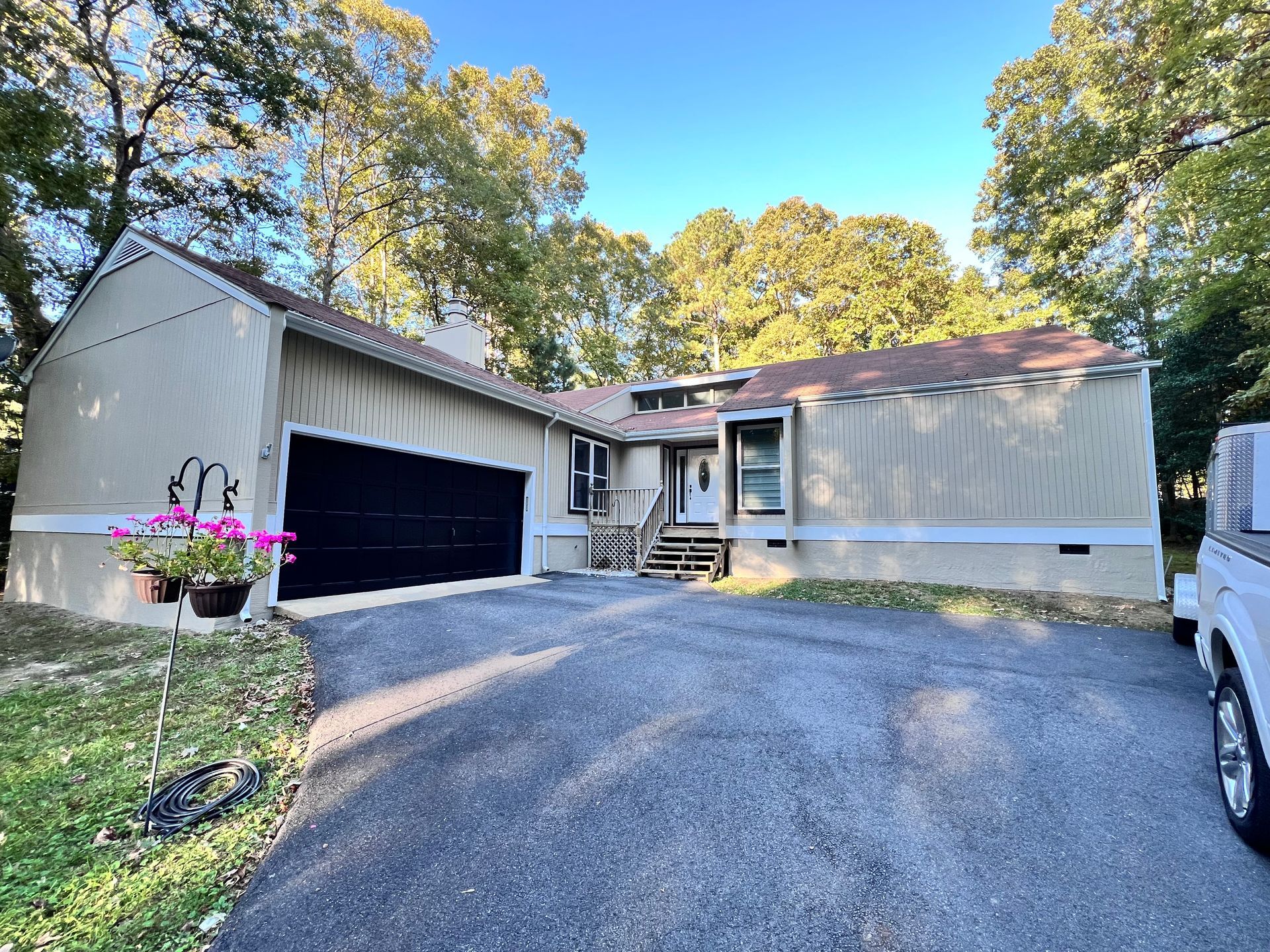 Single-story house with attached garage, driveway, and trees in front yard, viewed from the front.